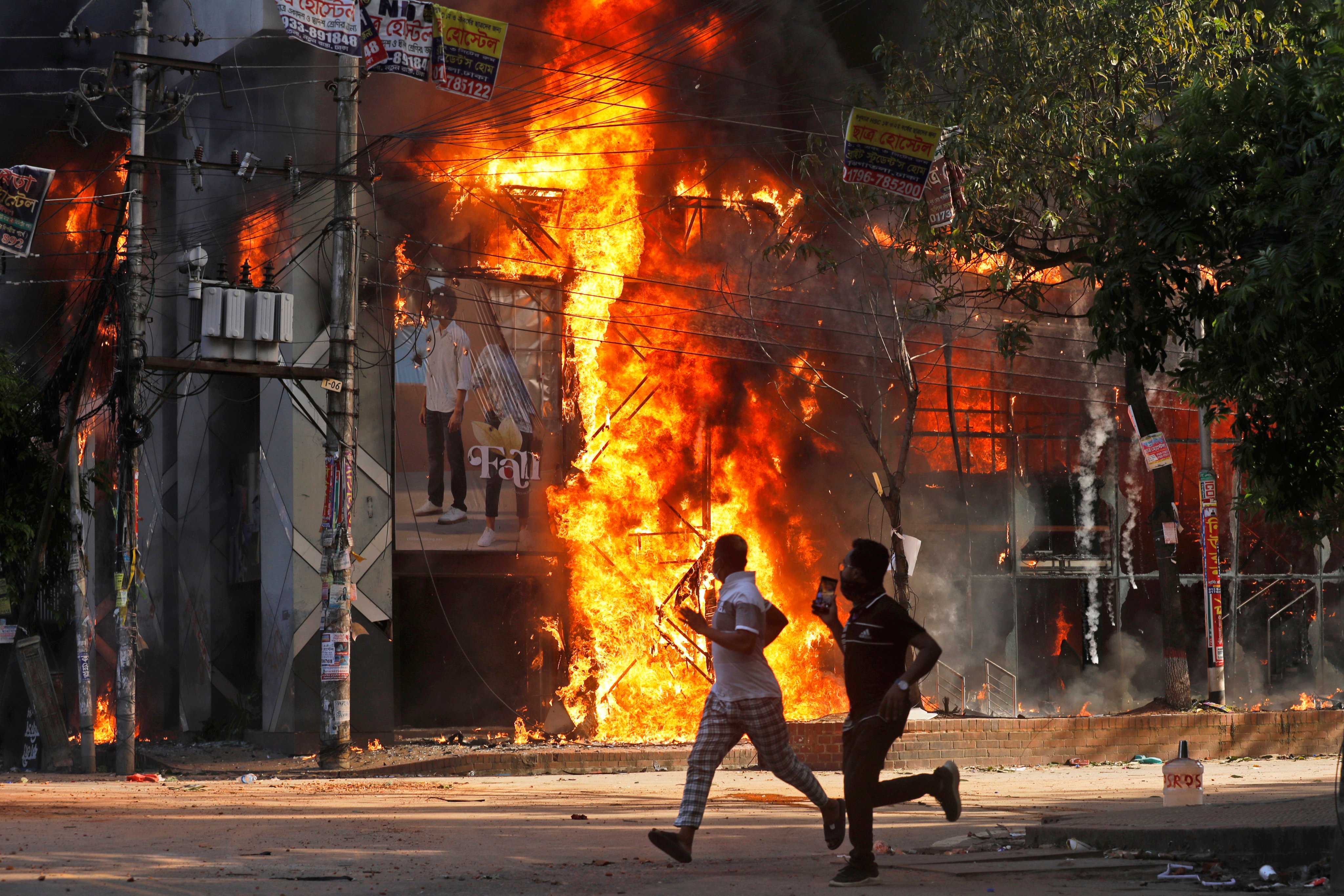 Men run past a shopping centre which was set on fire by protesters in Dhaka, Bangladesh. Photo: AP