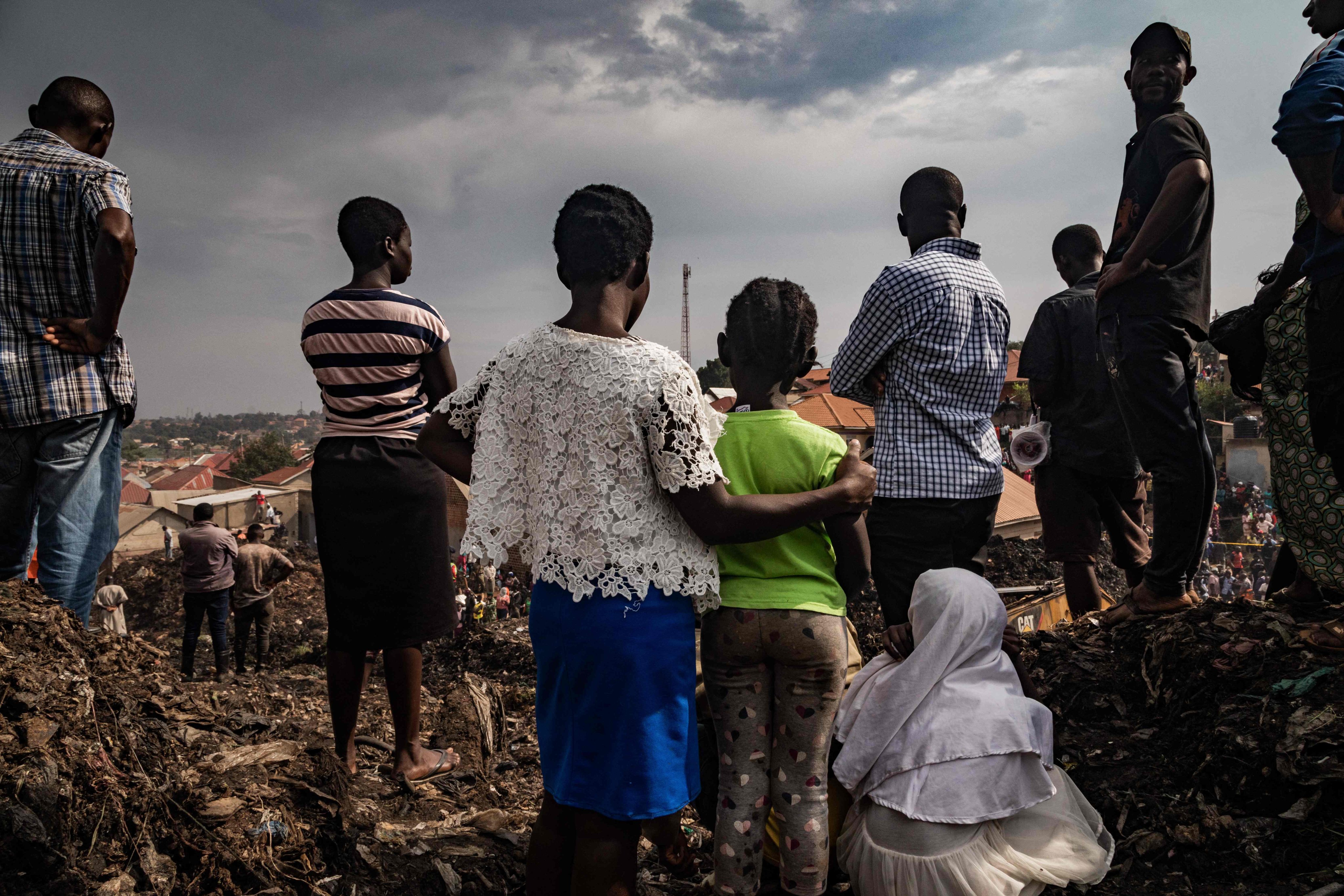 People look on as an excavator helps search for people trapped under debris after part of a massive rubbish dump collapsed in Kampala, Uganda on Saturday. Photo: AFP