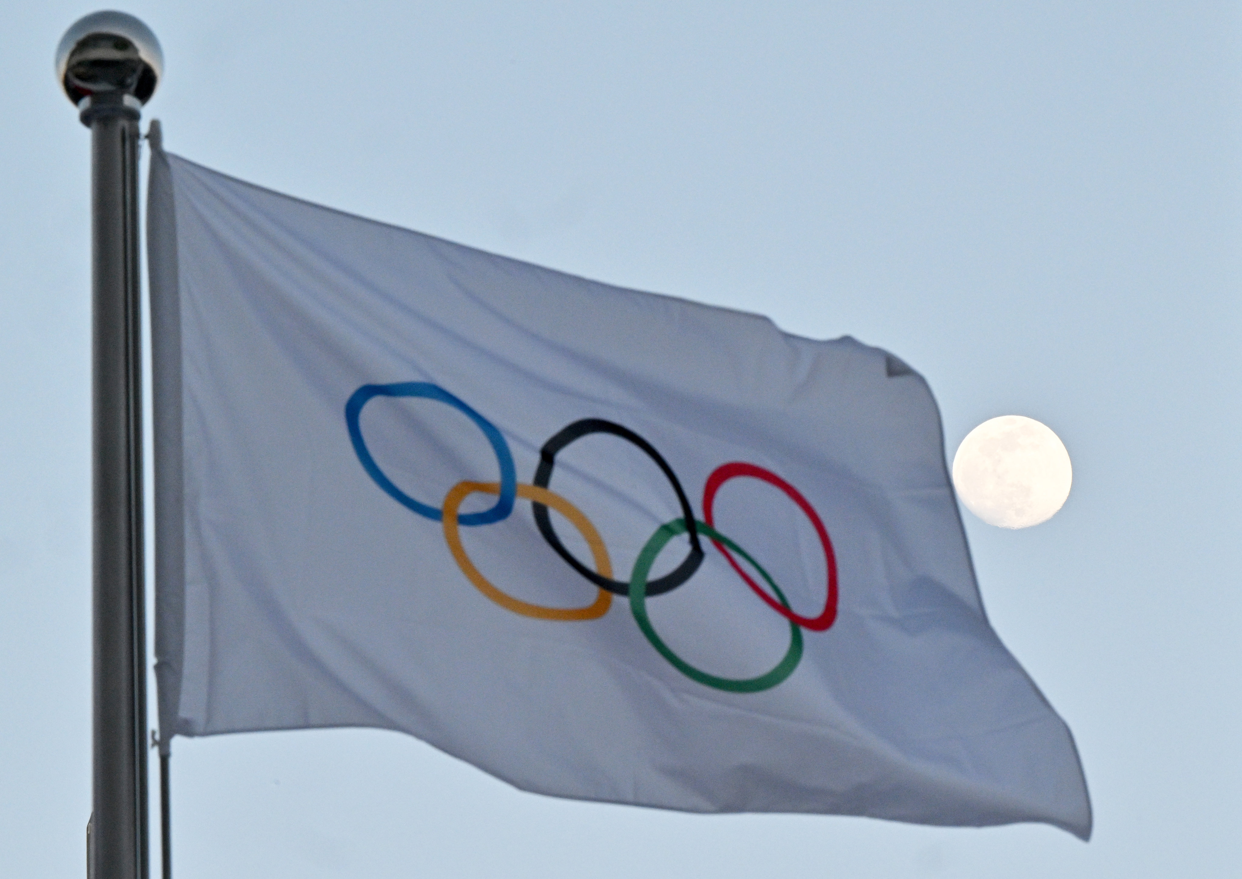 The moon can be seen behind the flag with the Olympic rings. Photo: dpa