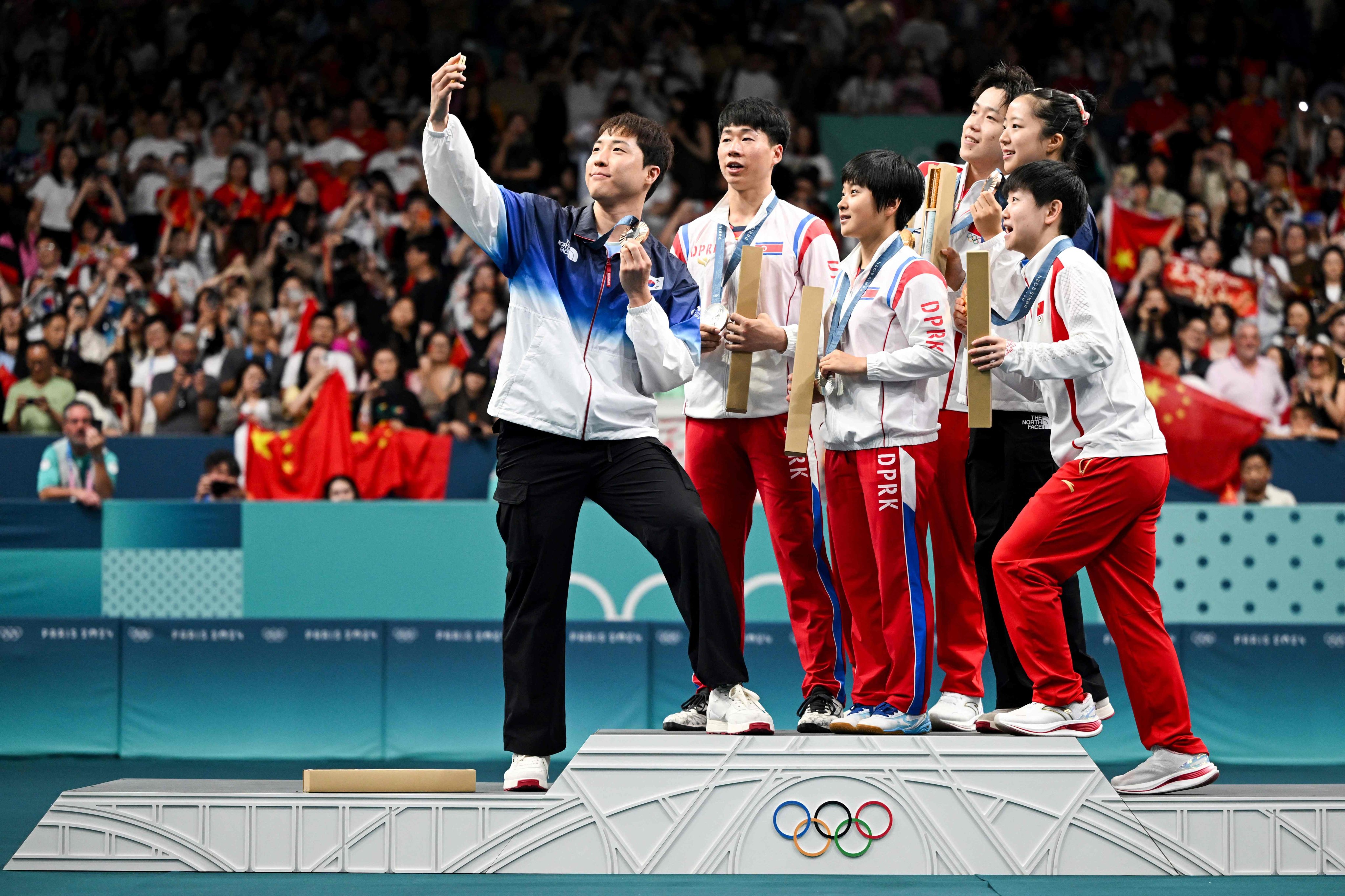 Medallists from South Korea, North Korea and China gather on the podium for a selfie at the end of their mixed table tennis doubles competition at the Summer Olympic Games at the South Paris Arena in Paris on July 30. Photo: AFP