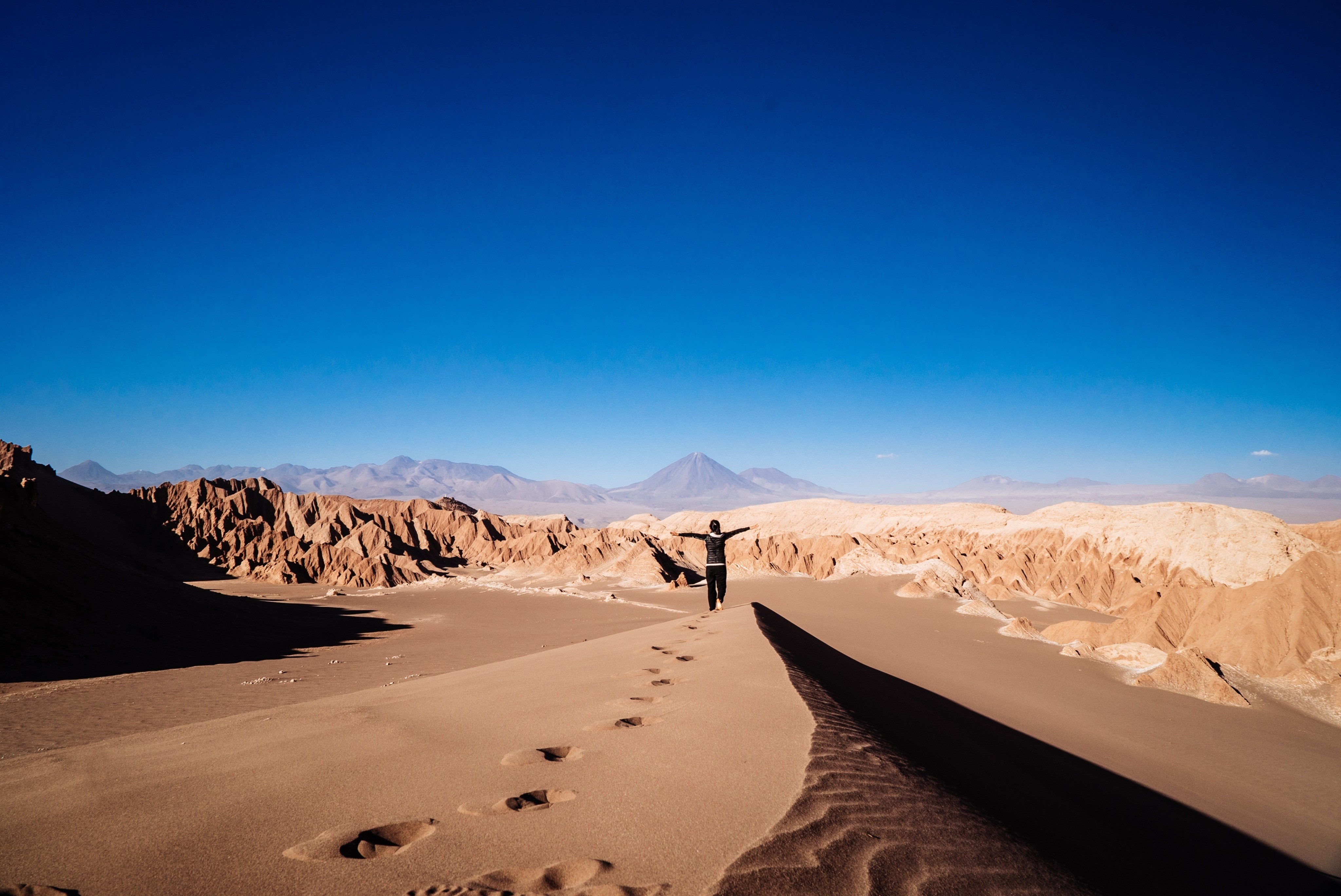 Sandboarding in the Atacama Desert, Chile. A lone adventurer climbs a vast sand dune under the blazing sun, capturing the essence of adventure and natural beauty. Shutterstock