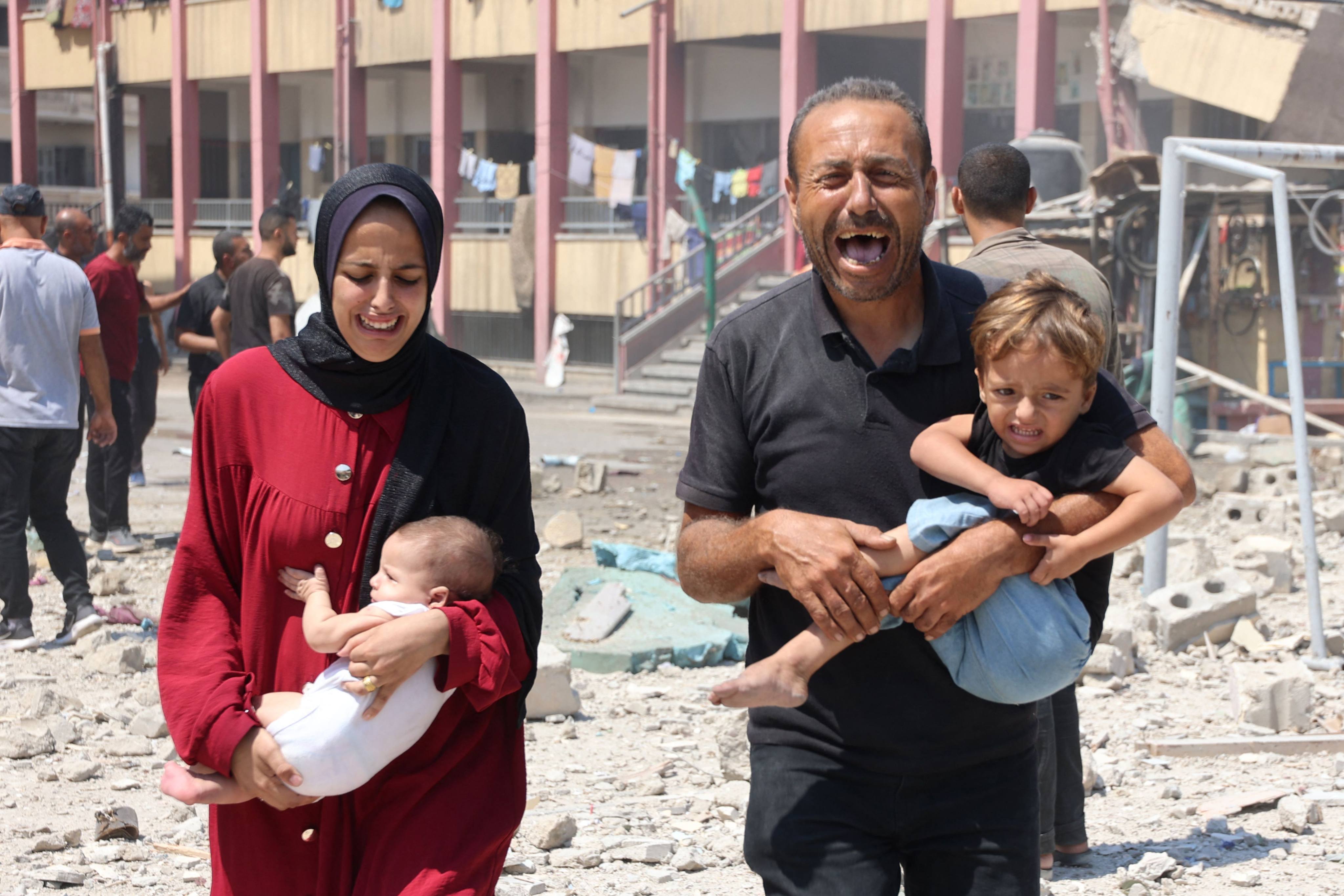 Palestinians carry their children as they flee after an Israeli strike on a school, housing displaced Palestinians, in central Gaza City on August 20. Photo: AFP