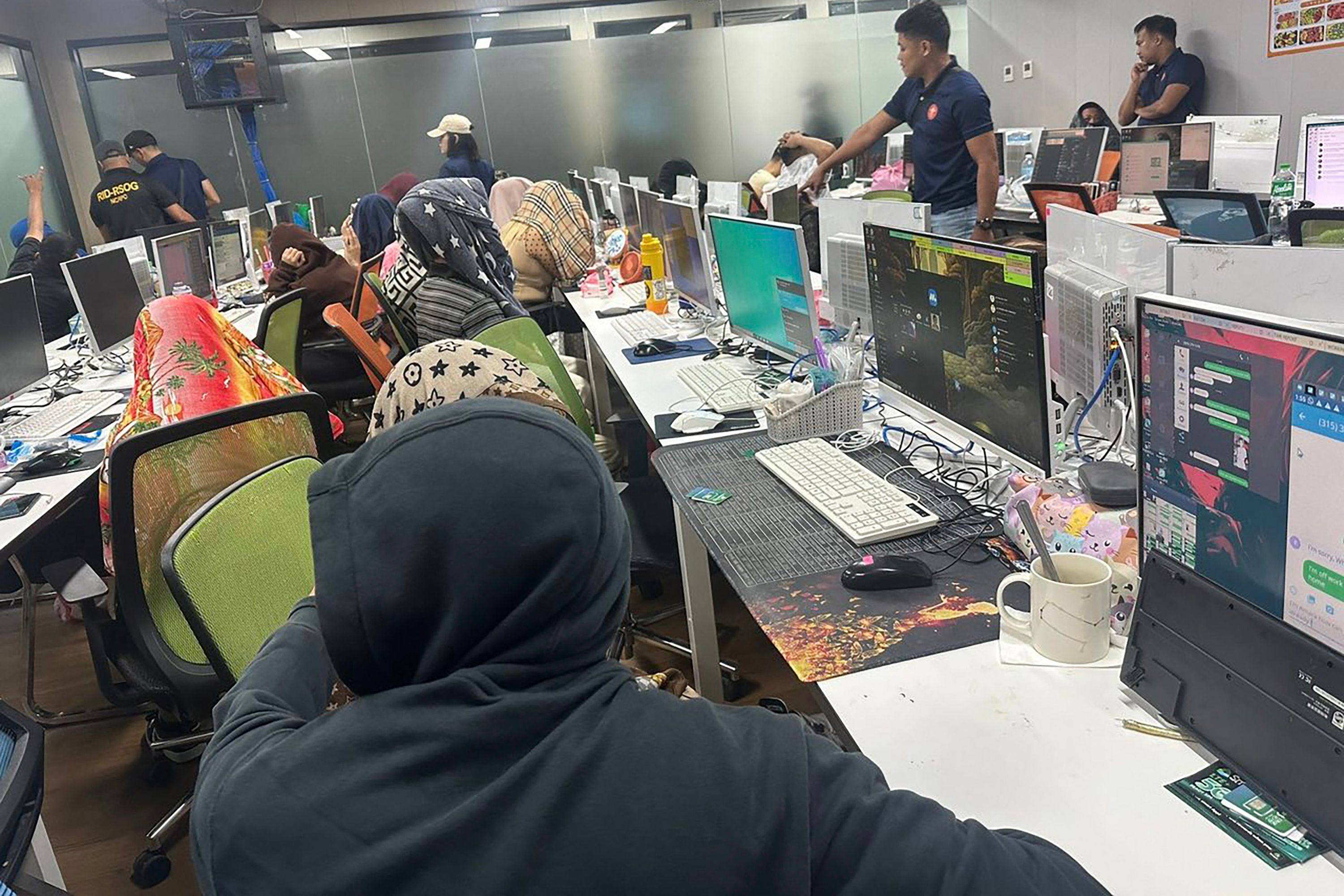 Philippine policemen watch as employees of a Chinese-run scam farm cover their faces during a raid at an office tower in Manila. Photo: AFP