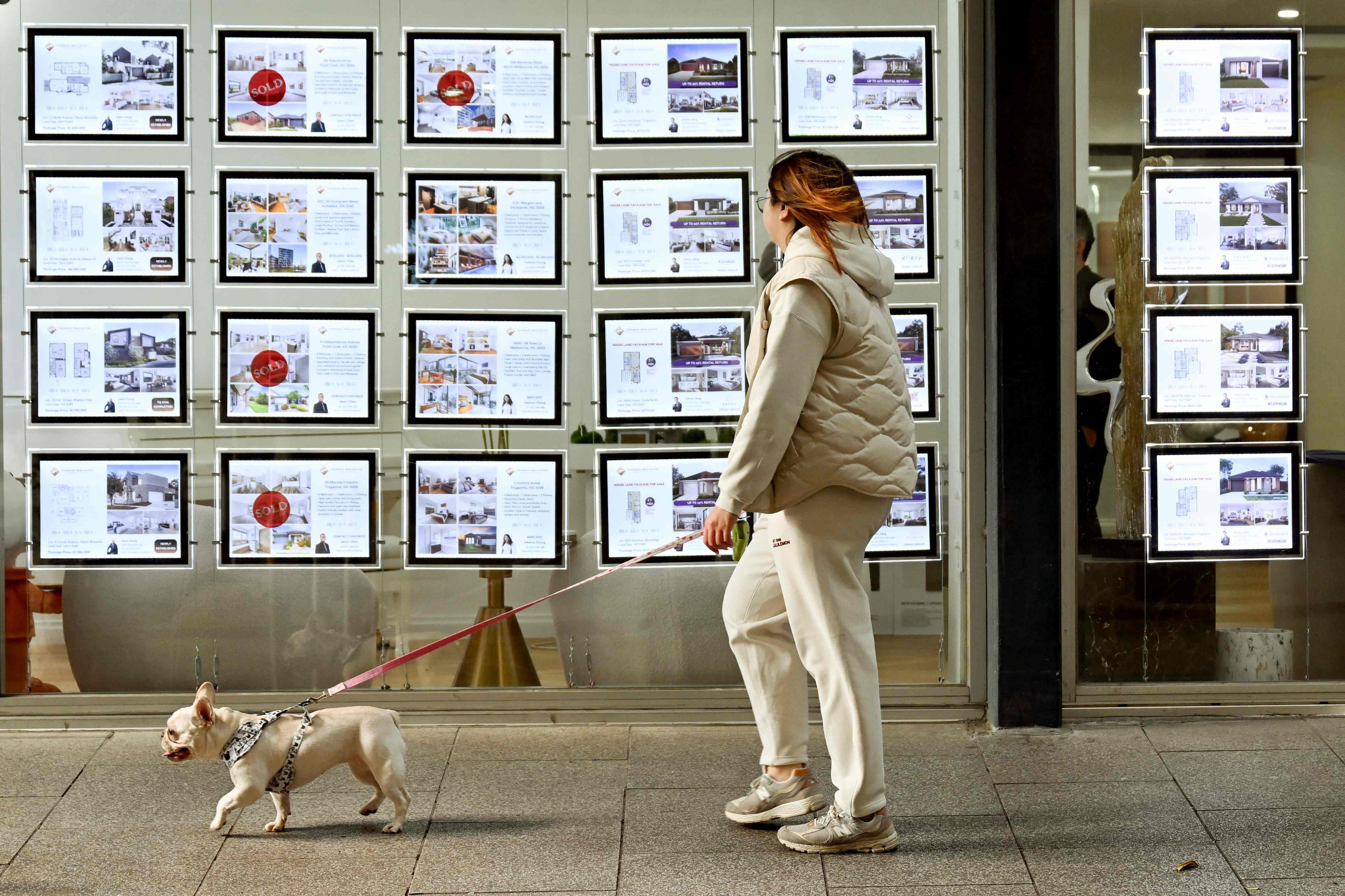 A woman and her dog walk past a property agent’s in Melbourne on August 6. The Reserve Bank of Australia kept borrowing costs at a 12-year high earlier this month, and even discussed the possibility of a further increase, because of persistently elevated inflation. Photo: AFP