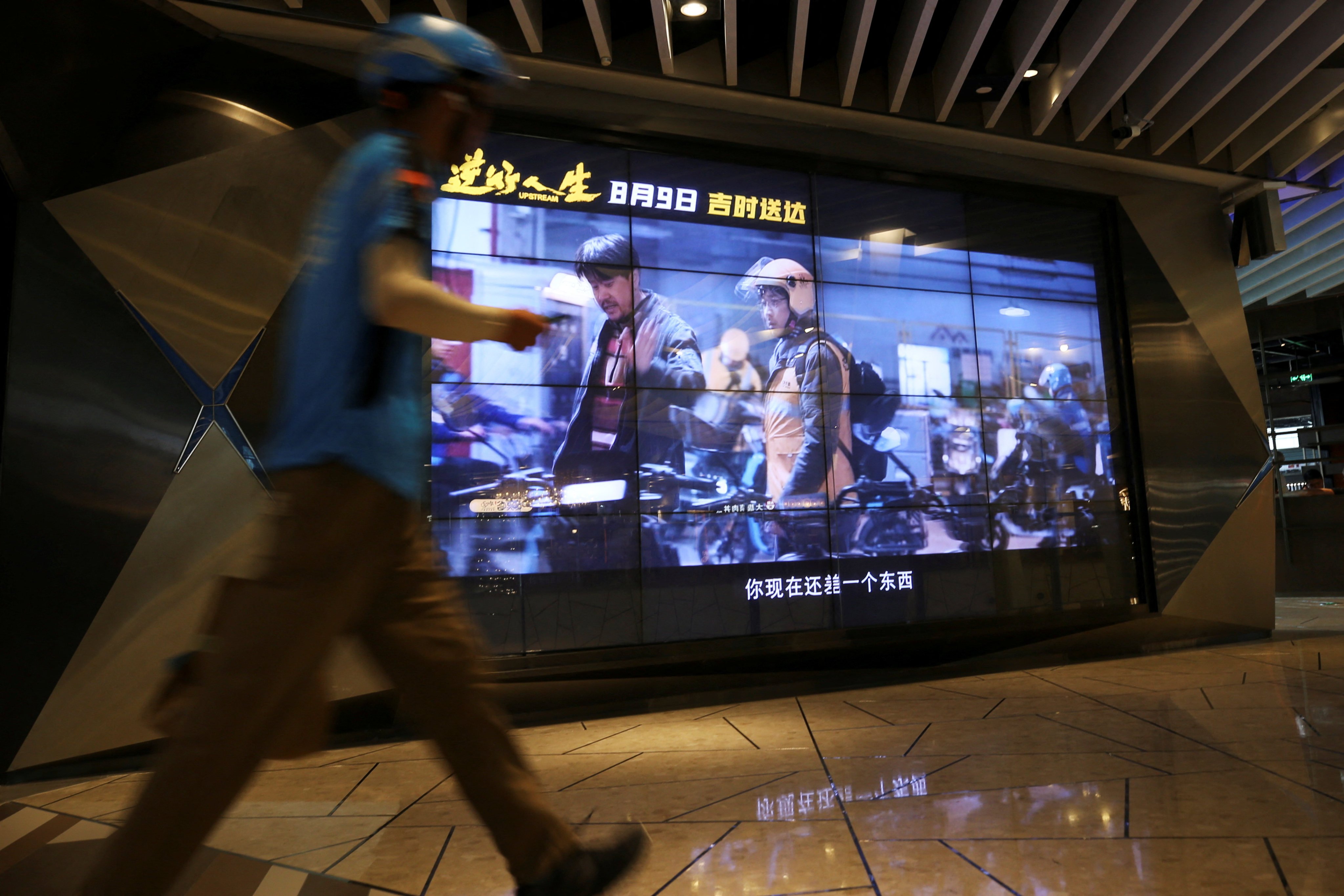 A delivery worker walks past a screen showing a trailer for the Chinese film “Upstream” at a mall in Shanghai, on August 14. Photo: Reuters