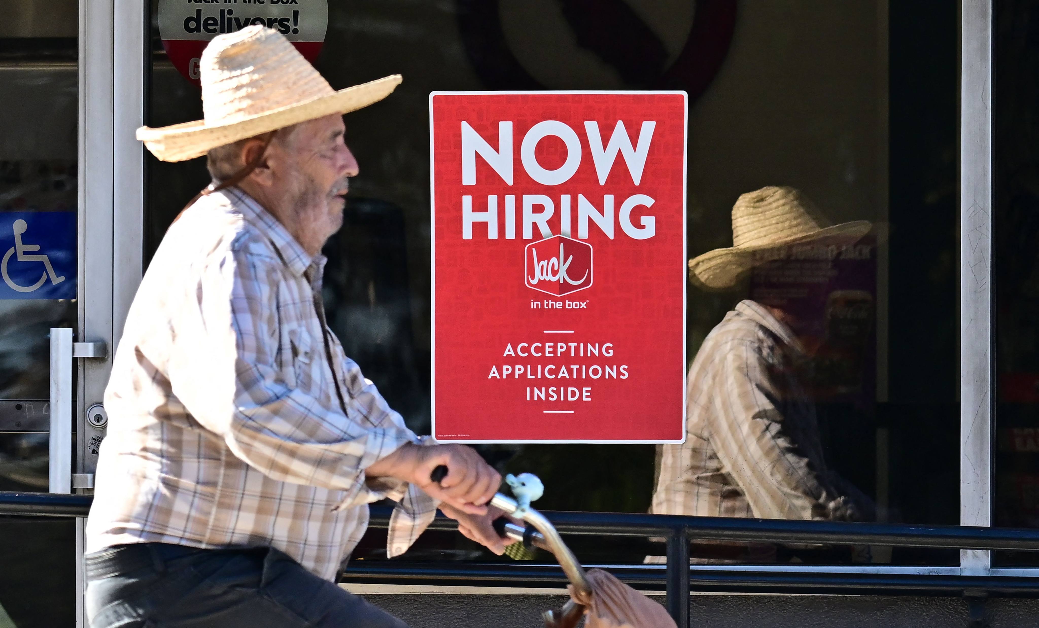 A cyclist rides past a “Now Hiring” sign posted on a business storefront in San Gabriel, California, on August 21. US figures for the 12 months ending in March showed there were 818,000 fewer jobs than previously reported in the largest downward revision since 2009. Photo: AFP