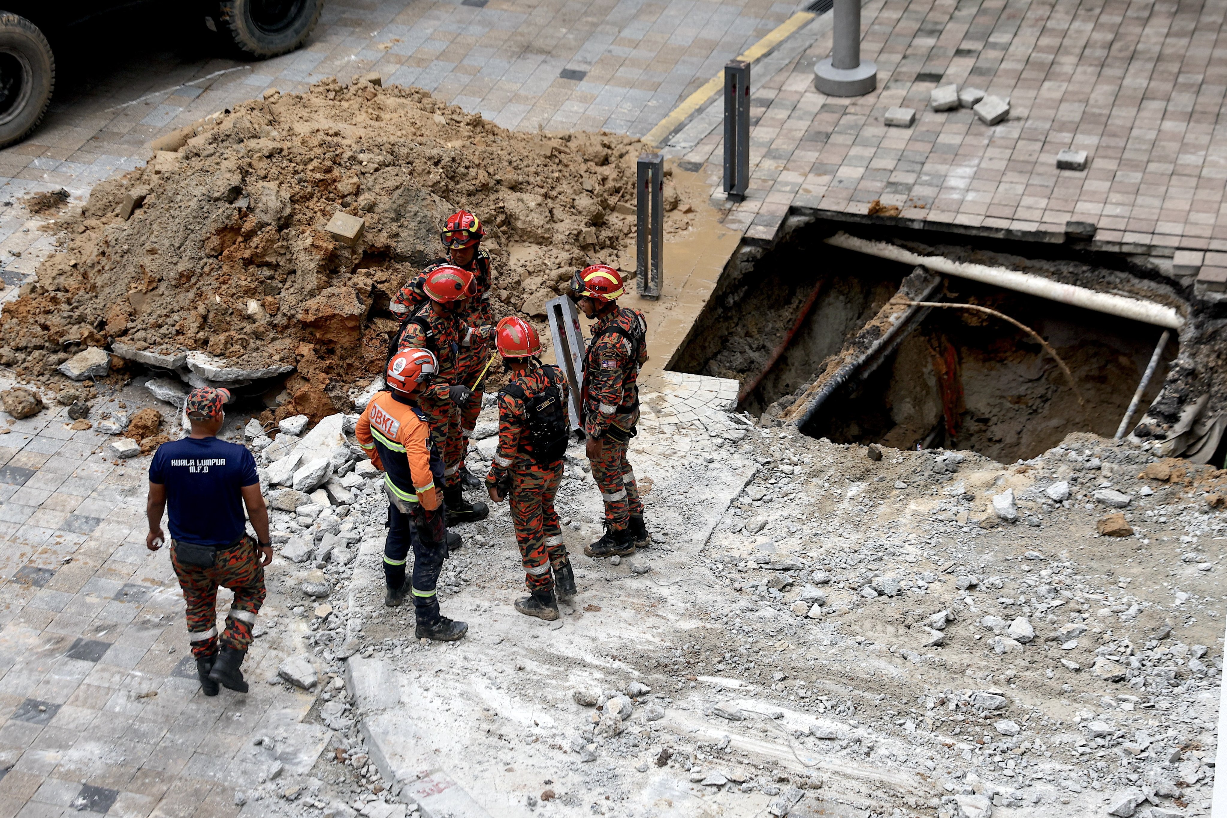 Malaysia Fire and Rescue Department officers inspect the site where a woman fell into an eight-metre-deep sinkhole in Kuala Lumpur on August 23. Photo: EPA-EFE