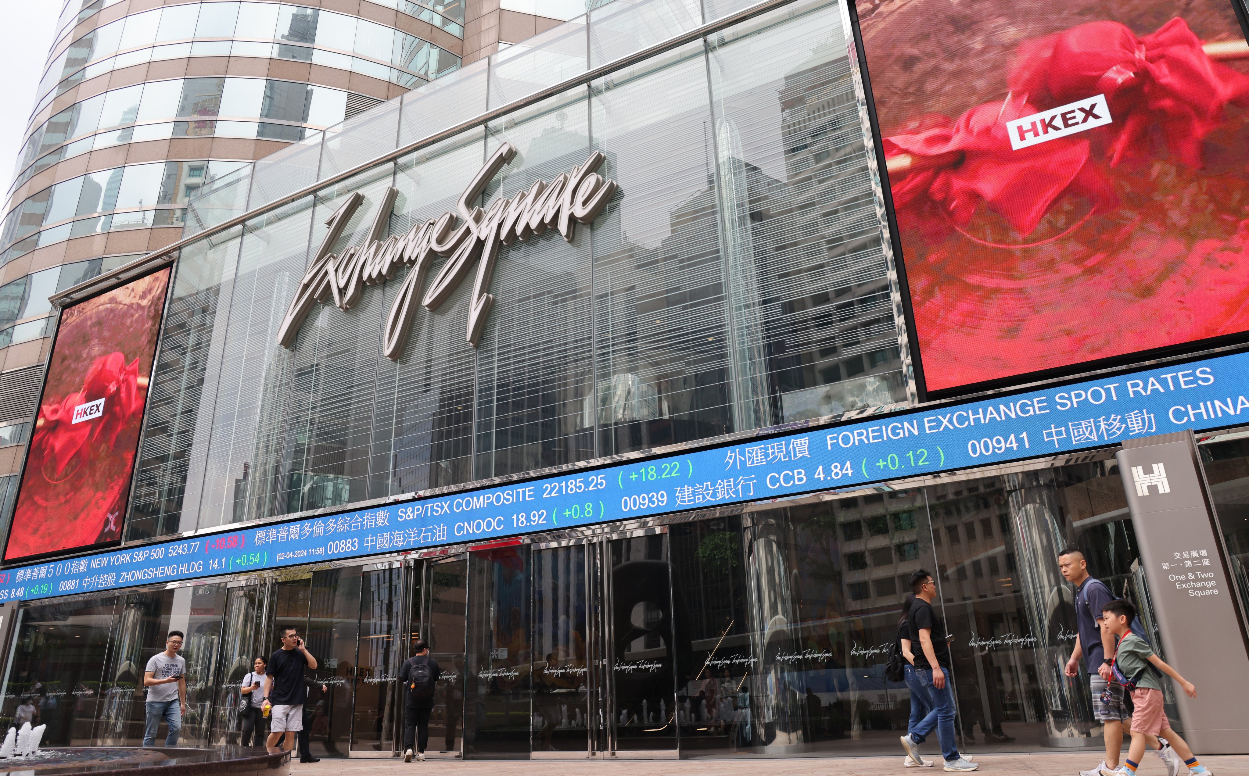 People walking past electronic boards outside the Exchange Square in Central in April 2024. Photo: Jelly Tse.