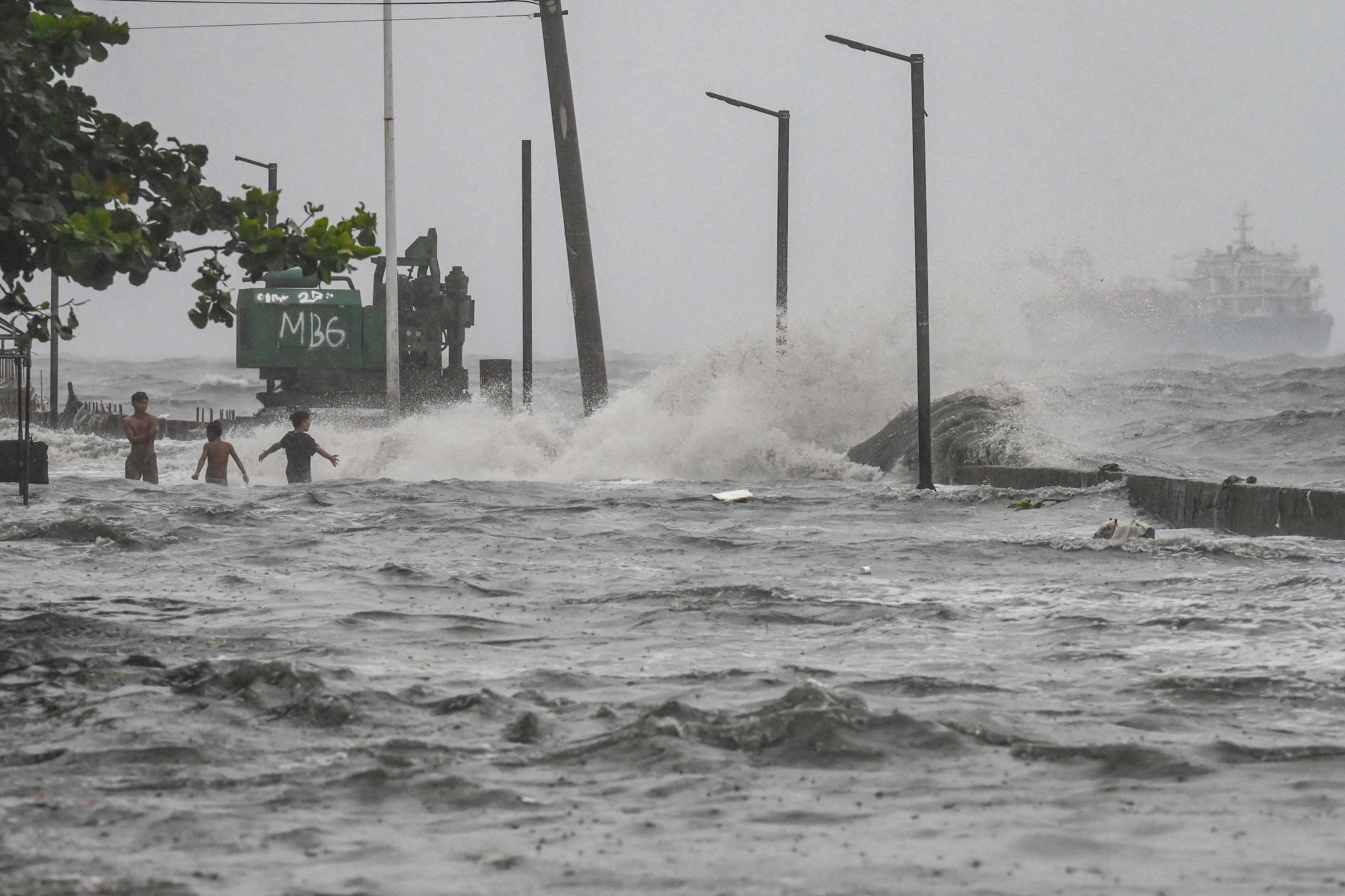 Youths wade through a storm surge along the Manila Bay coastline on Monday amid heavy rains brought by Tropical Cyclone Yagi. Photo: AFP