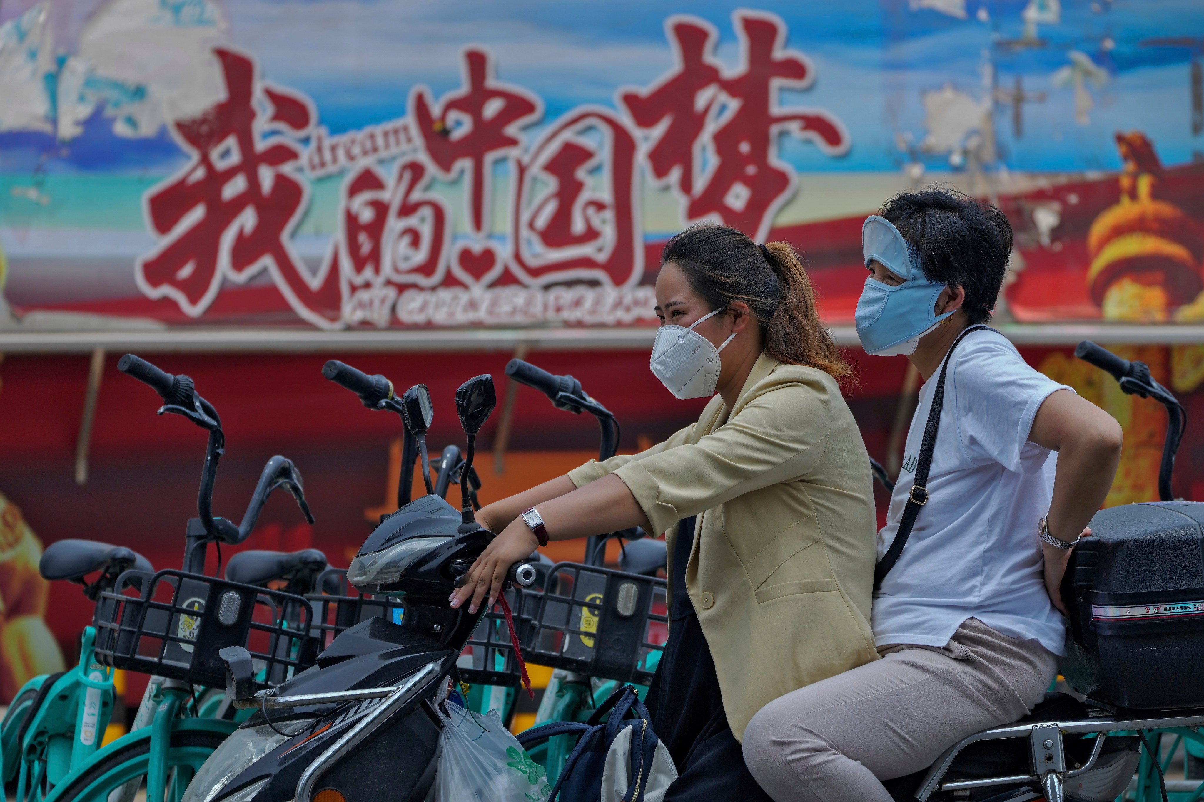 Women ride a scooter near a poster promoting the Chinese Dream in Beijing in June 2022. The Chinese government recognises that allowing wealth to be concentrated among the few is not in the people’s best interests. Photo: AP