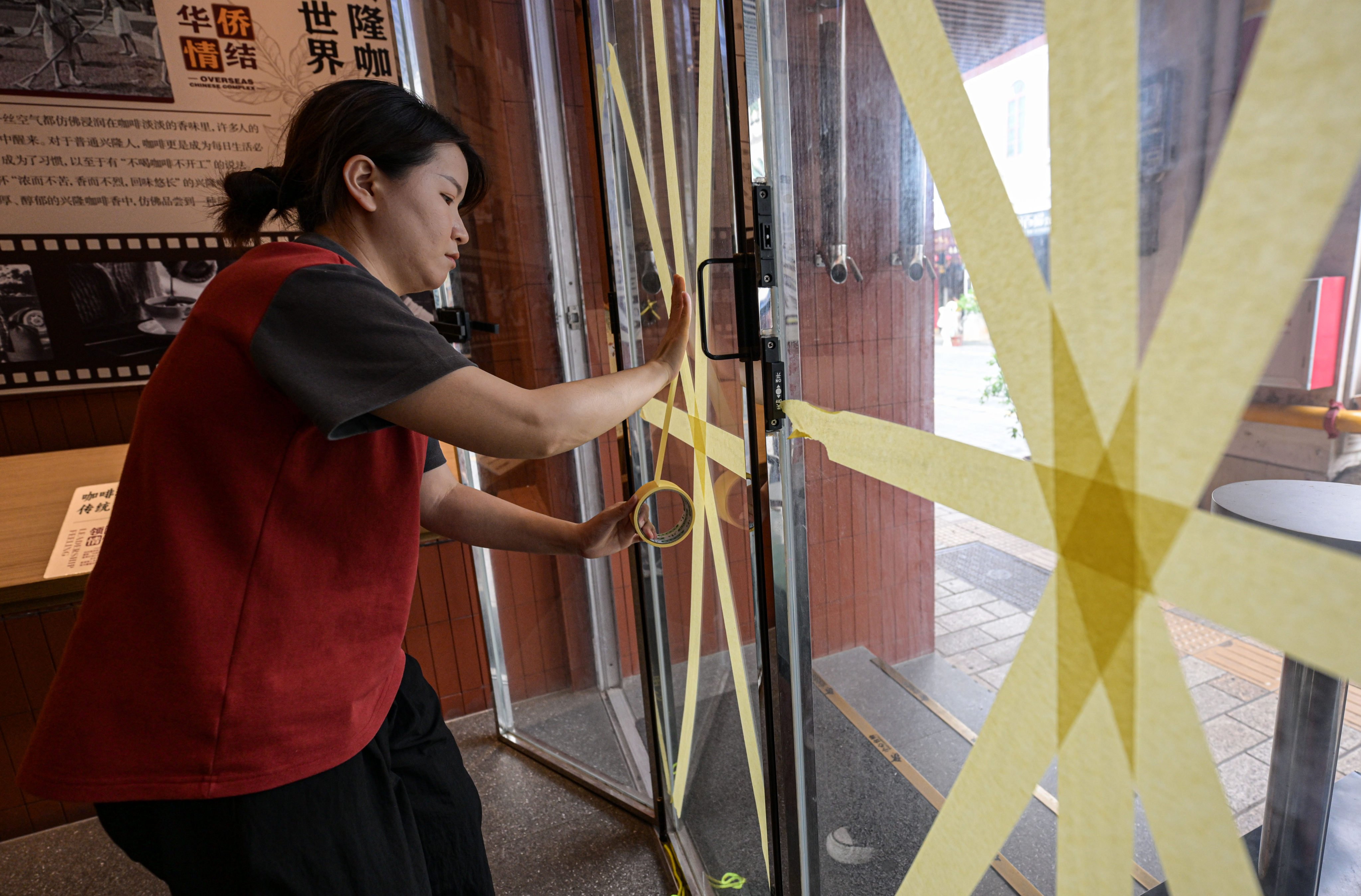 A cafe worker reinforces a glass window in Haikou on Thursday in preparation for Super Typhoon Yagi. Photo: Xinhua