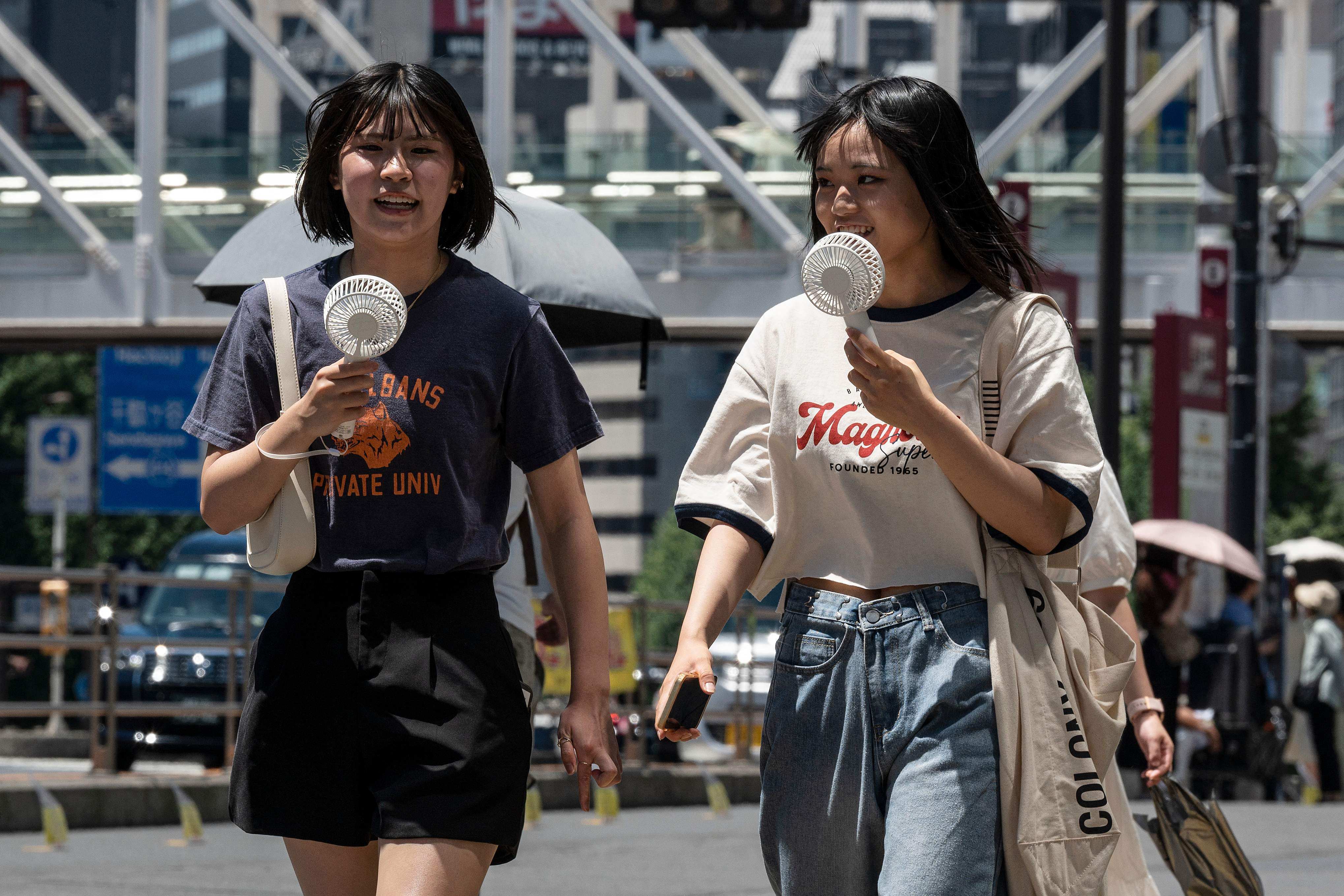 Young women using portable fans to seek relief from the heat while walking outside Tokyo’s Shinjuku station. Photo: AFP