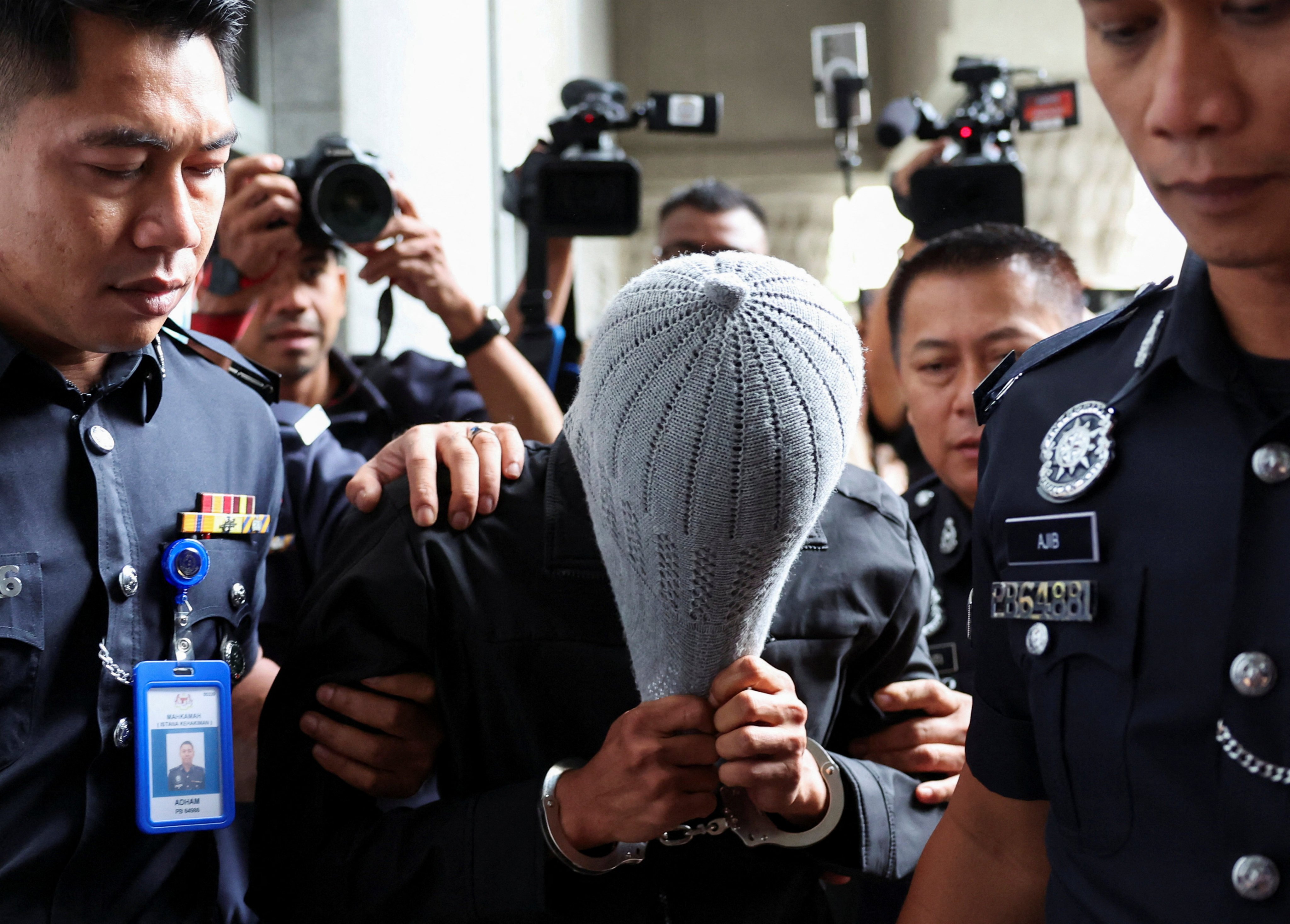 A member of Global Ikhwan Service and Business Holdings (GISB) covers his face as he is escorted by police officers after being charged at a court in Putrajaya, Malaysia on September 18. Photo: Reuters