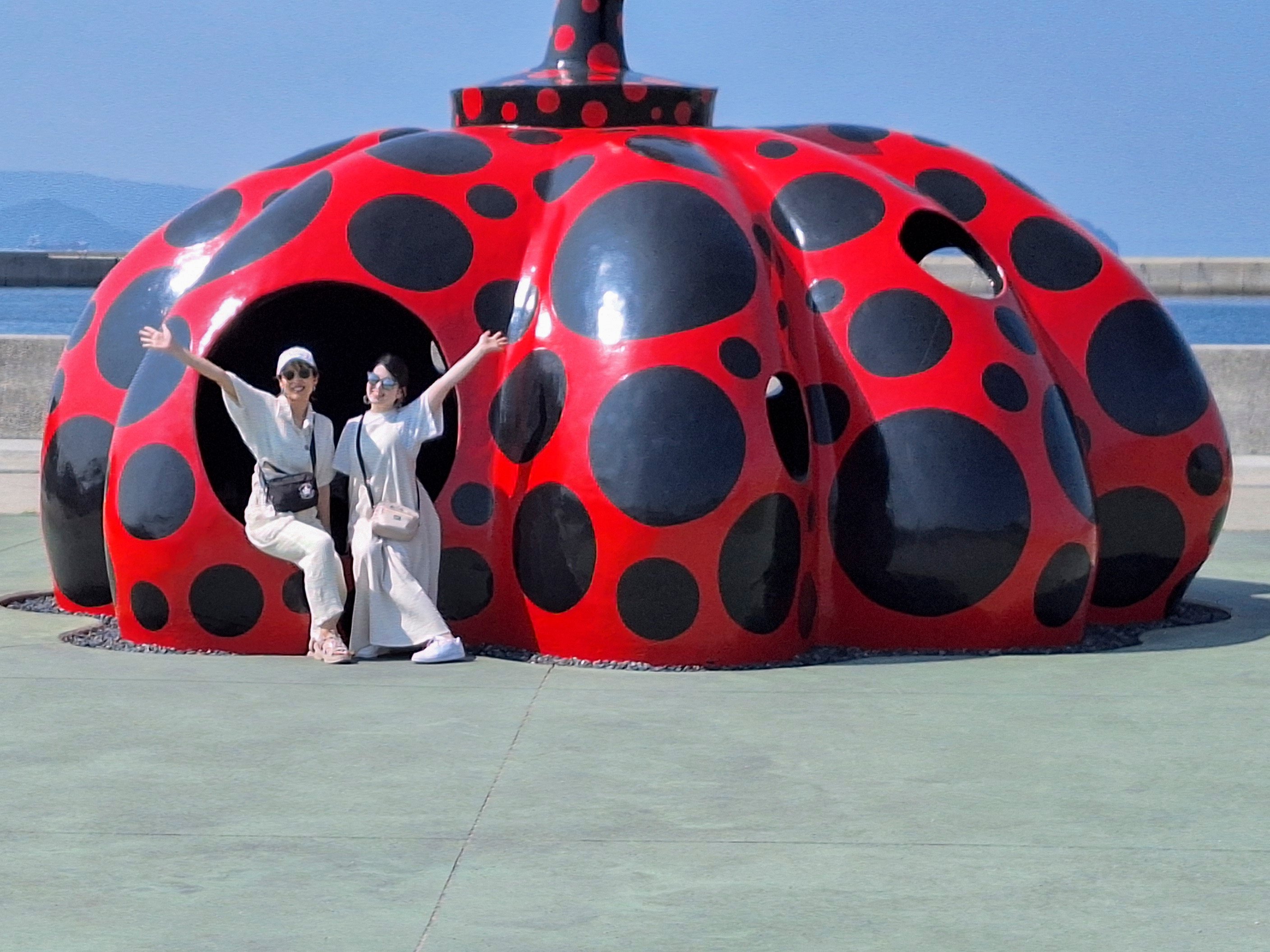 Two people pose for a photo seated on Red Pumpkin by Yayoi Kusama on Naoshima island, Takamatsu, Japan. Photo: Ed Peters