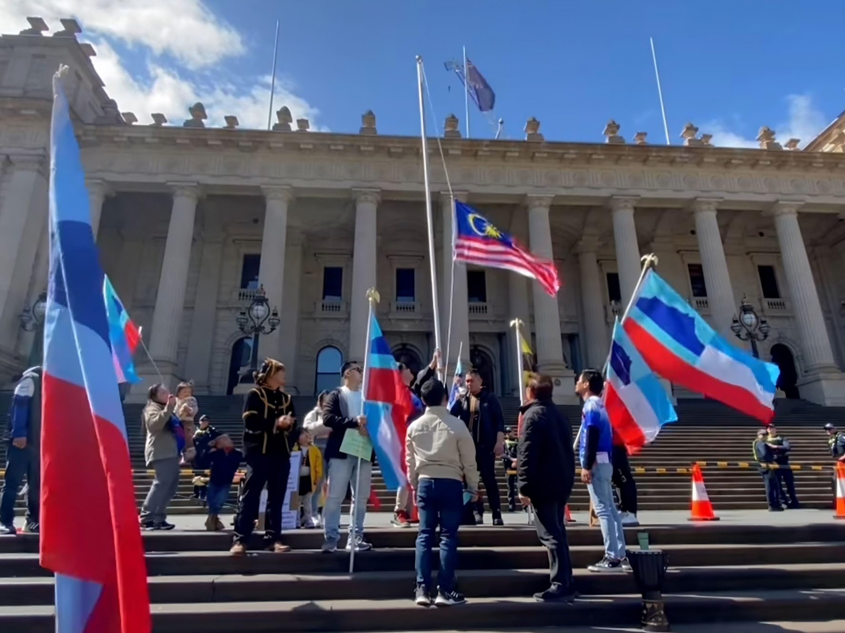 A still from the viral video shows the Malaysian national flag being lowered down a makeshift flagpole outside Parliament House in Melbourne, Australia. Photo: Facebook/MossesPA