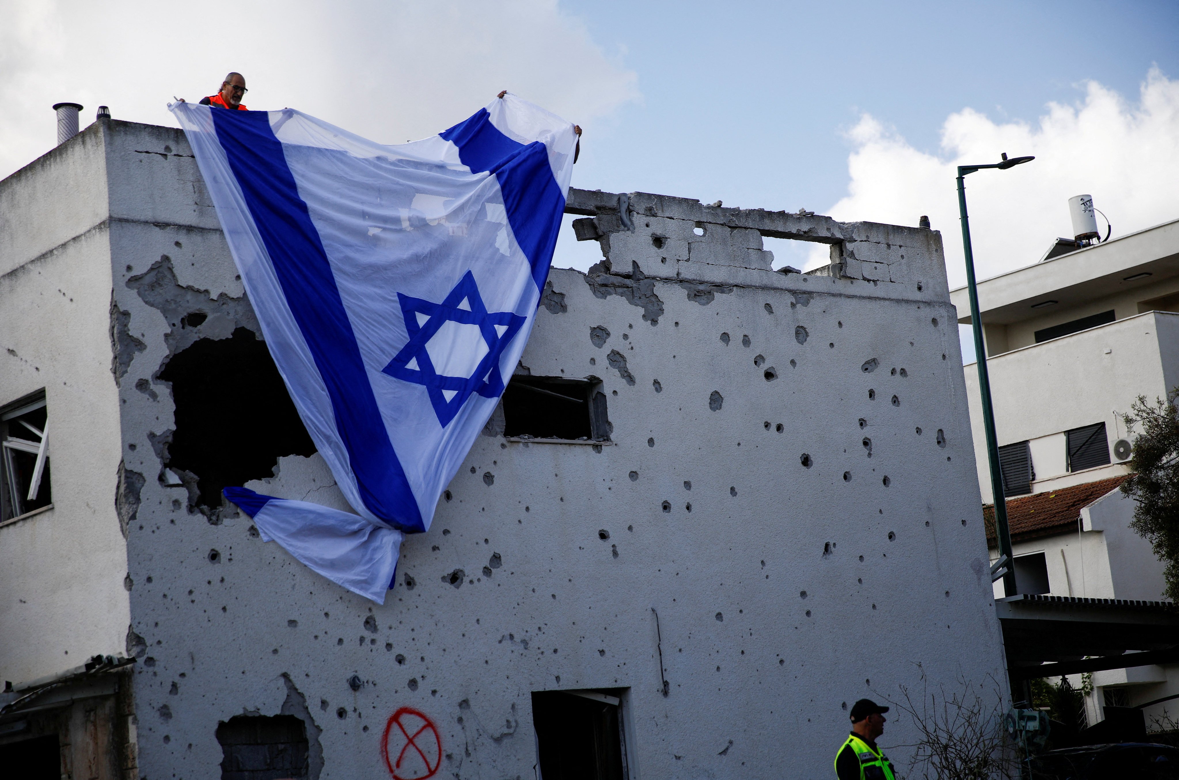 Israeli men hang an Israeli flag over a damaged building that was hit by a rocket from Lebanon, in Kiryat Bialik, Israel. Photo: Reuters