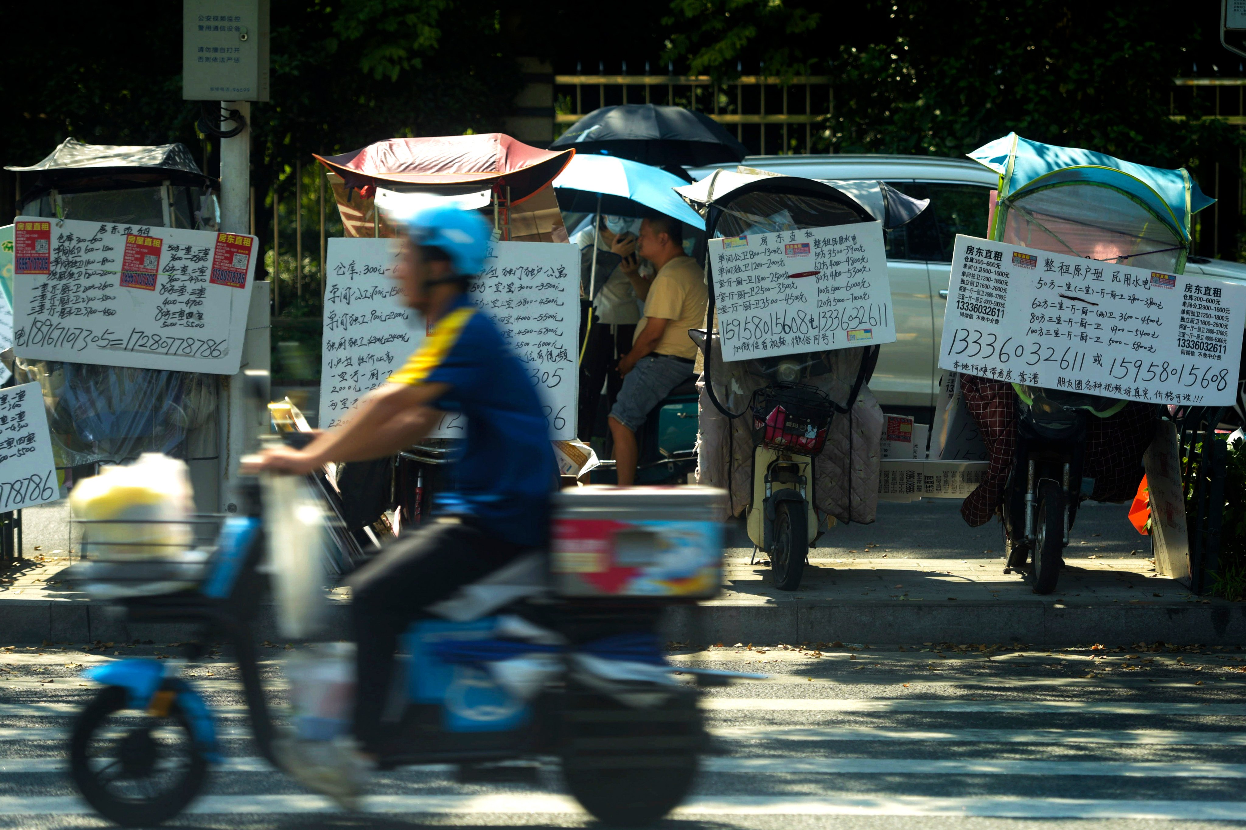 A motorist passes by placards showing properties for lease on electric scooters parked along the sidewalk in Hangzhou in east China’s Zhejiang province in August 2024. Photo: AP