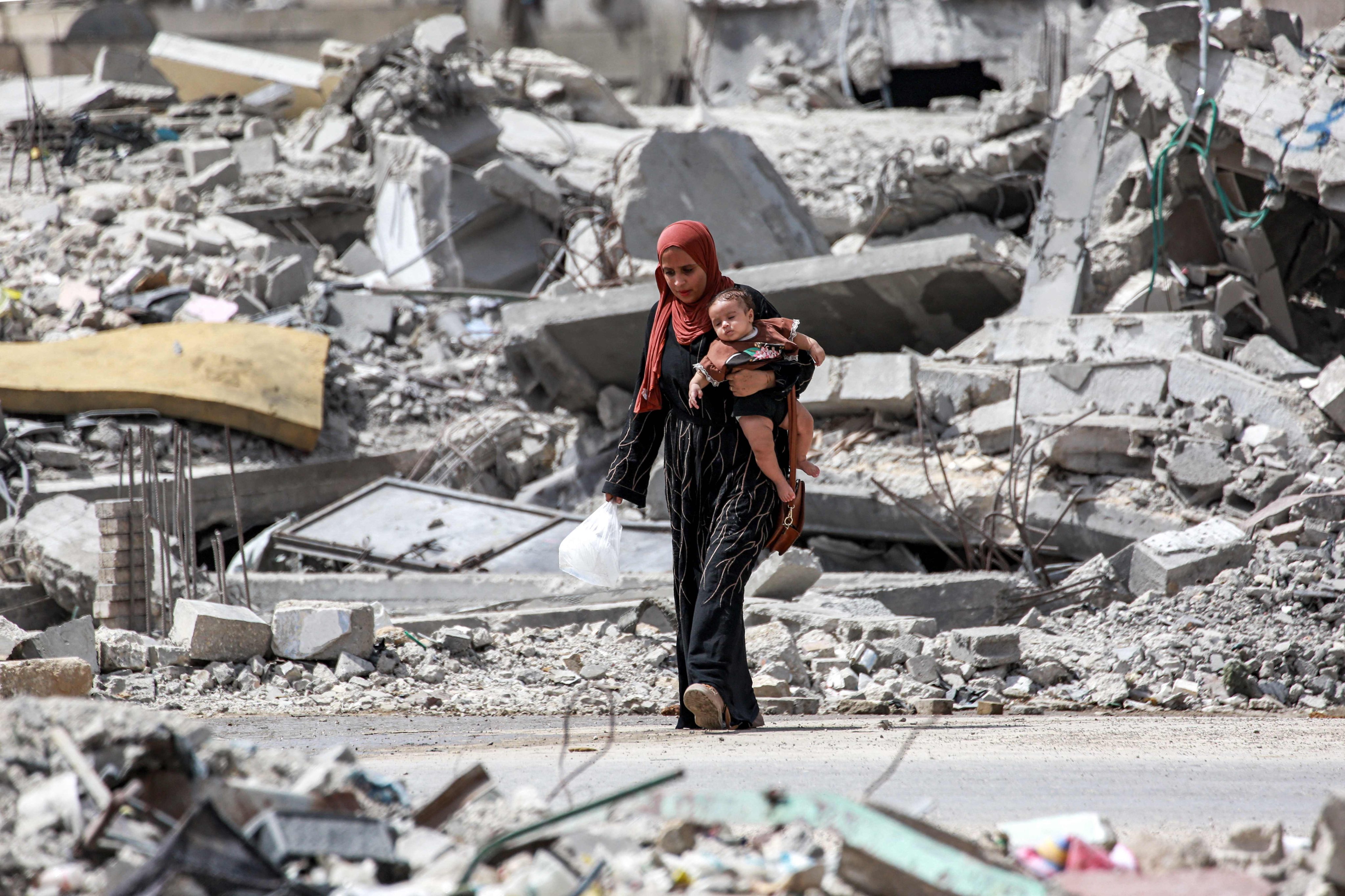 A woman walks with an infant past the rubble of a collapsed building in Khan Yunis in the southern Gaza Strip on September 16, 2024 amid the ongoing war in the Palestinian territory between Israel and Hamas. Photo: AFP