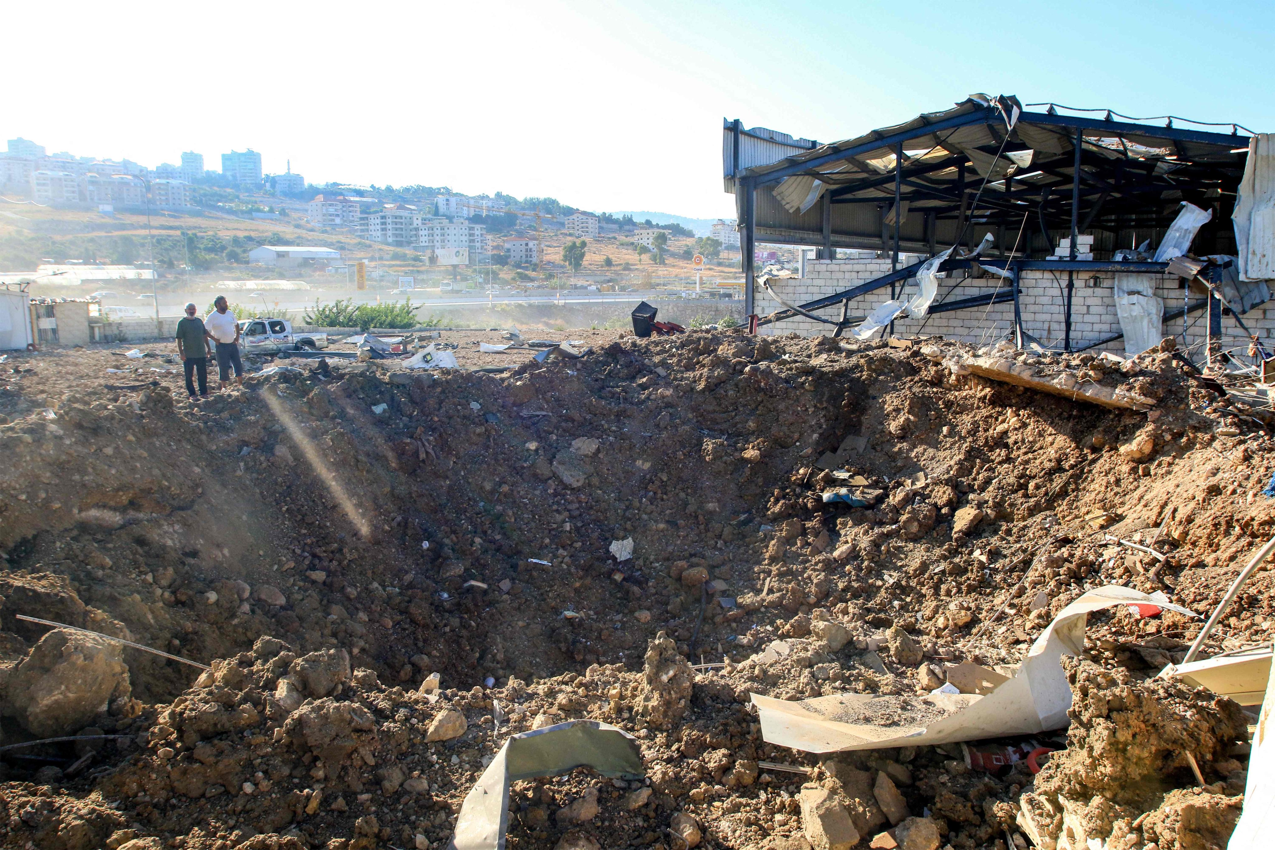 People stand by an impact crater next to a destroyed warehouse at the site of an Israeli air strike in Jiyeh along the highway linking Beirut to the southern Lebanese city of Sidon on September 25. Photo: AFP