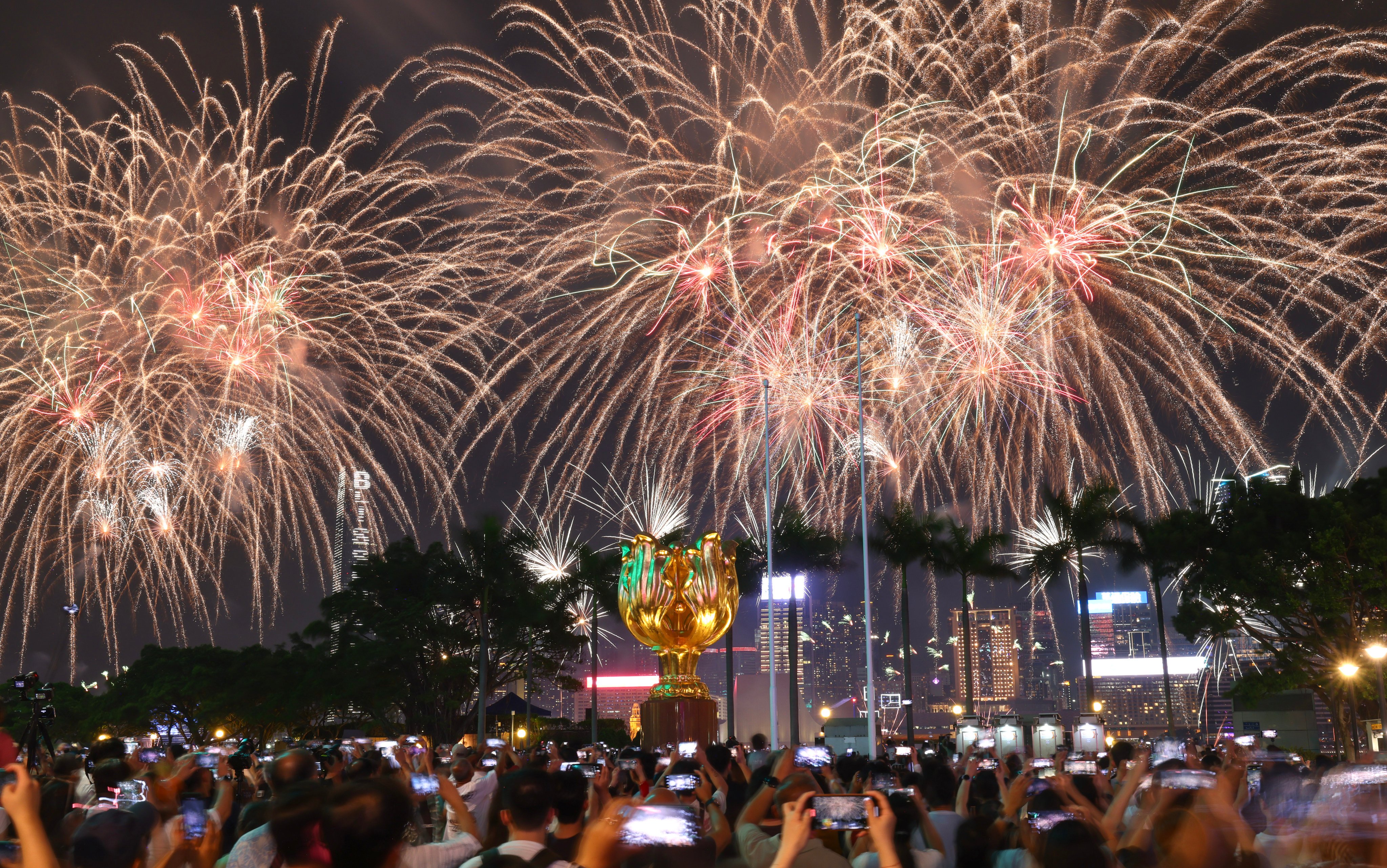 People take photographs of a firework display over Victoria Harbour to celebrate National Day at Golden Bauhinia Square in Wan Chai on October 1.  Photo: Dickson Lee