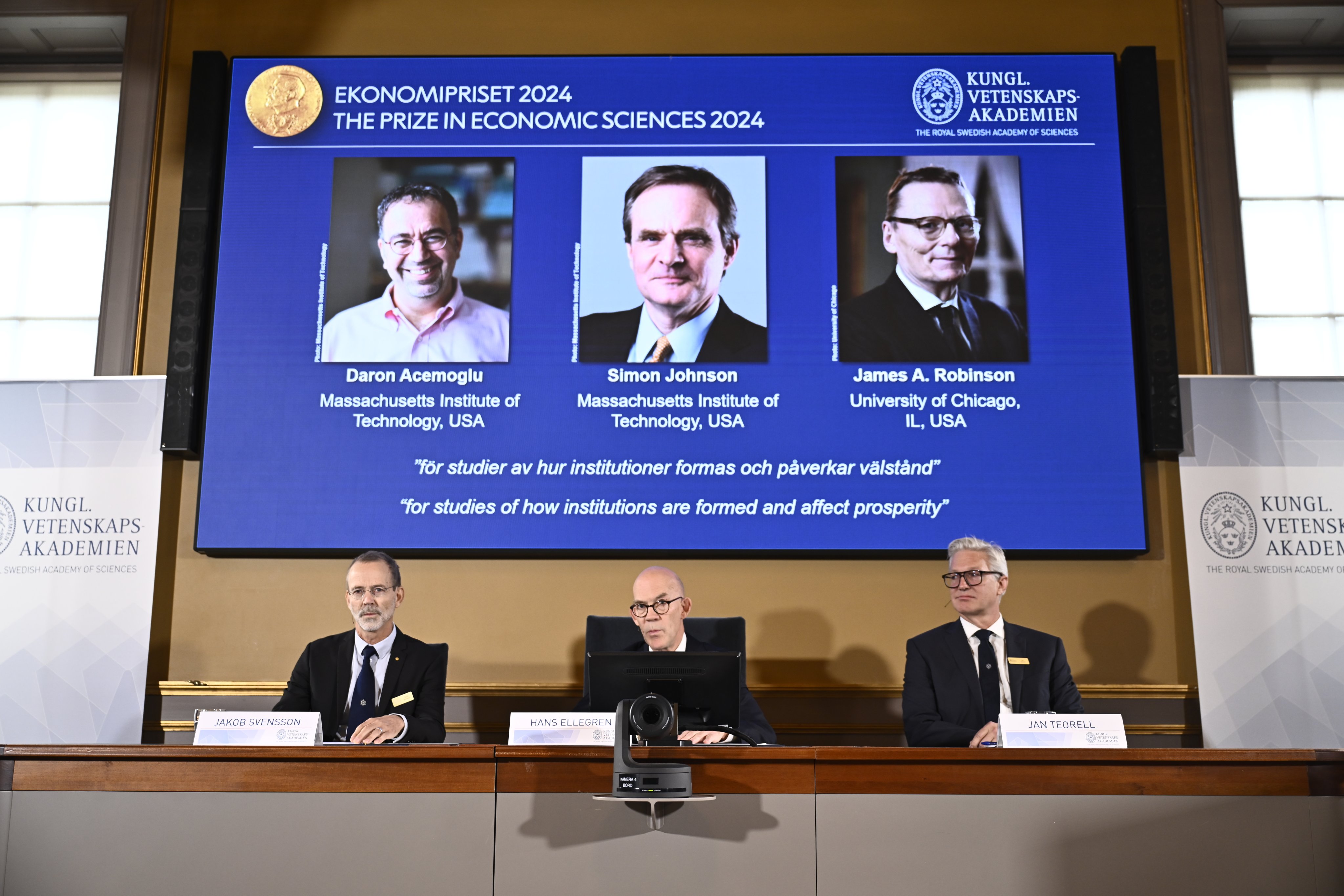 Members of the Nobel assembly announce the 2024 prize in economics, awarded to Daron Acemoglu, Simon Johnson and James A Robinson, seen on screen, during a press conference in Stockholm on Monday. Photo: EPA-EFE