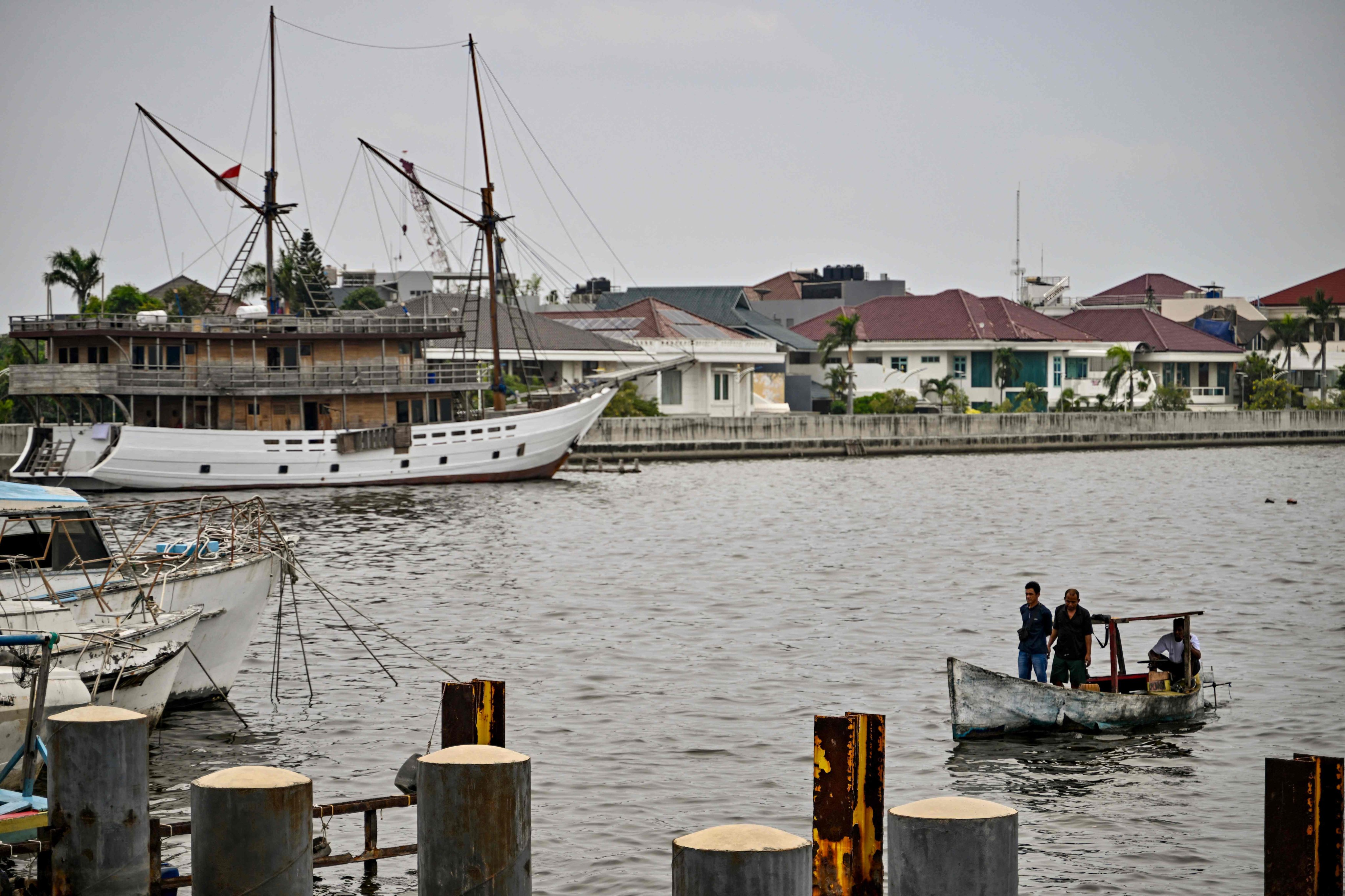 Boats on the water are seen beside a sea wall, holding back waters from residences built on land below sea level, along the northern coast of Jakarta, Indonesia. Photo: AFP