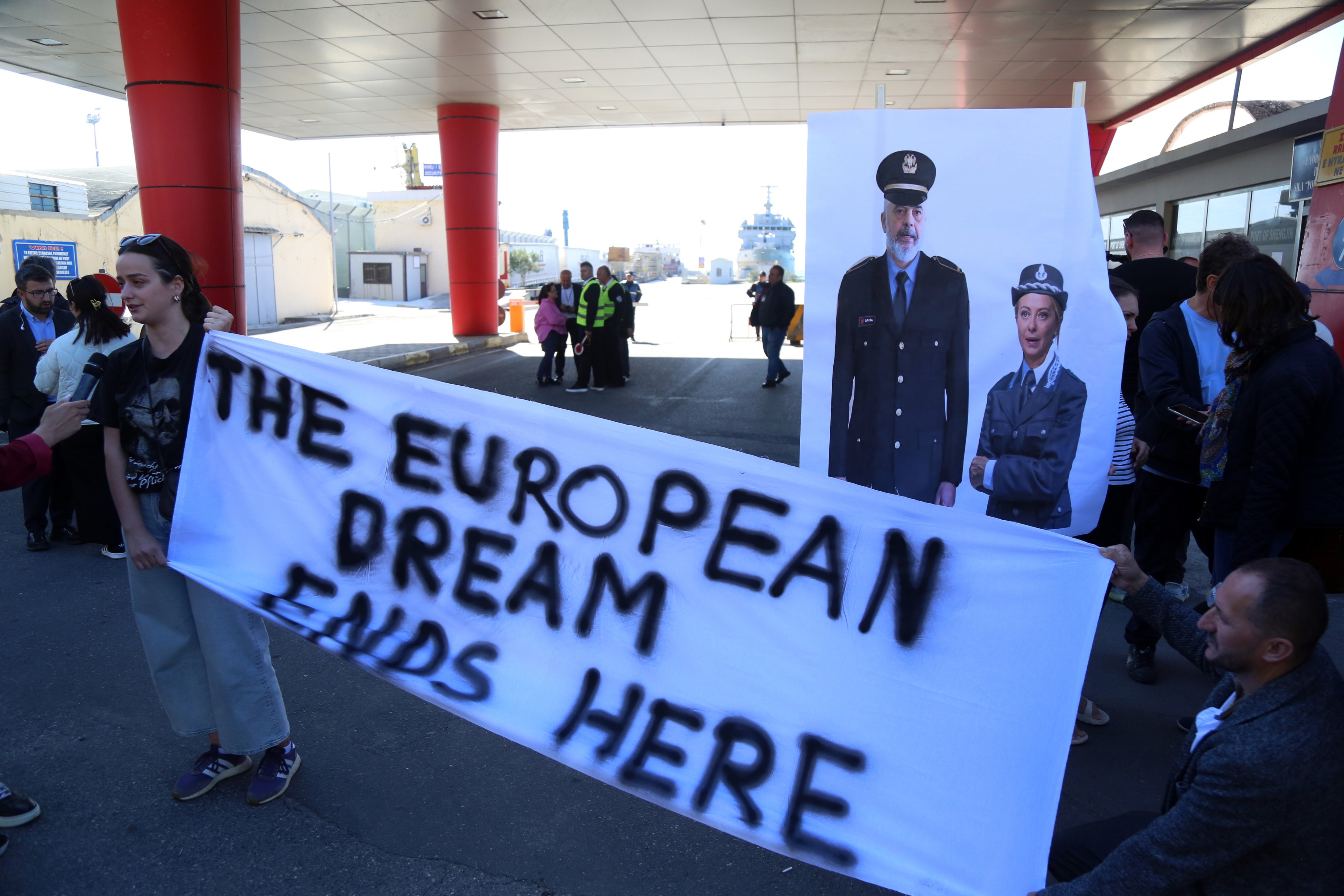 Activists hold a banner depicting Italian Prime Minister Giorgia Meloni and Albanian Prime Minister Edi Rama wearing police uniforms, as the first group of migrants intercepted in Italian waters arrive at Shengjin, Albania. Photo: EPA-EFE