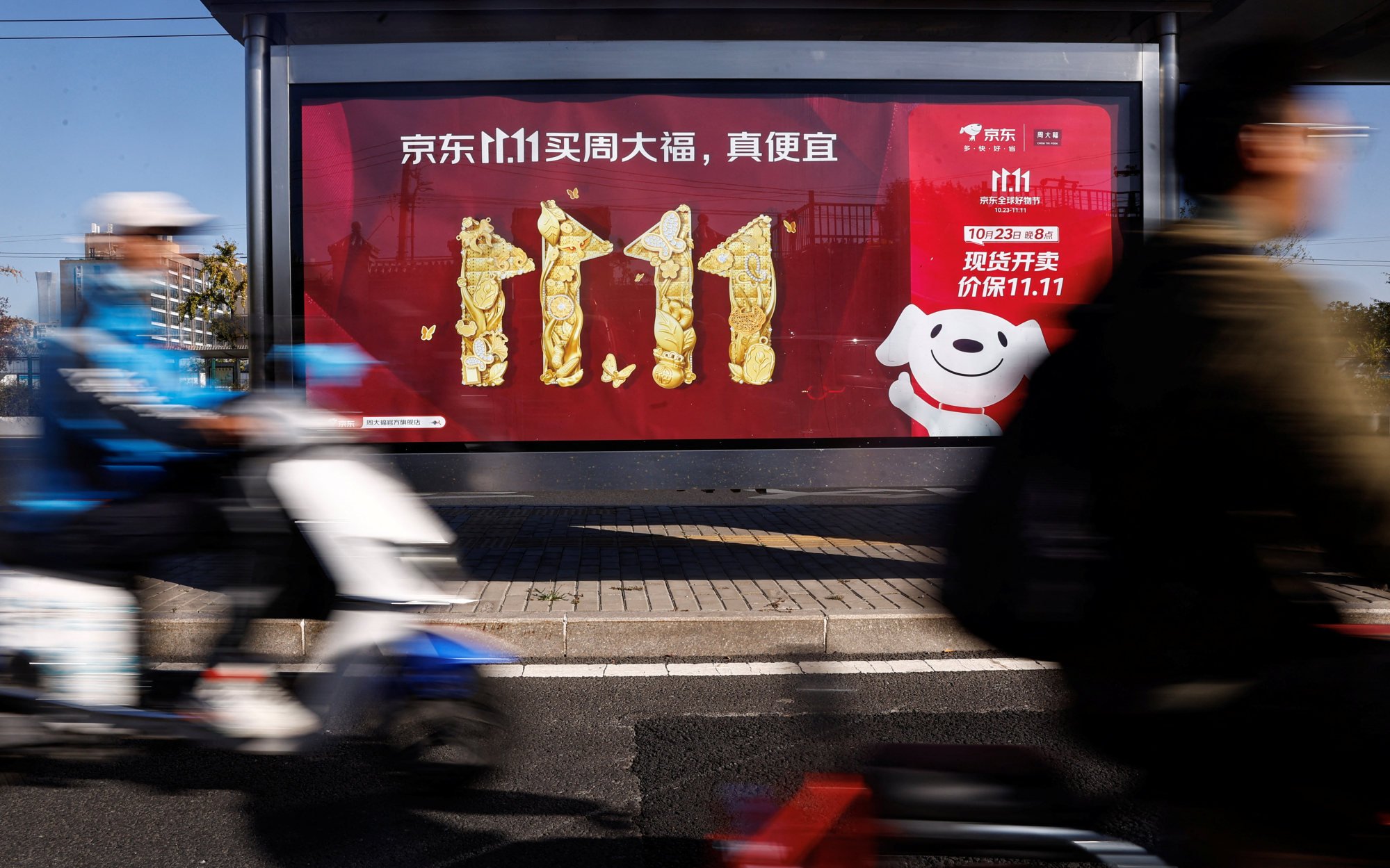 People on scooters ride past a JD.com advertisement in Beijing promoting the firm’s campaign for the annual Singles’ Day shopping festival. Photo: Reuters