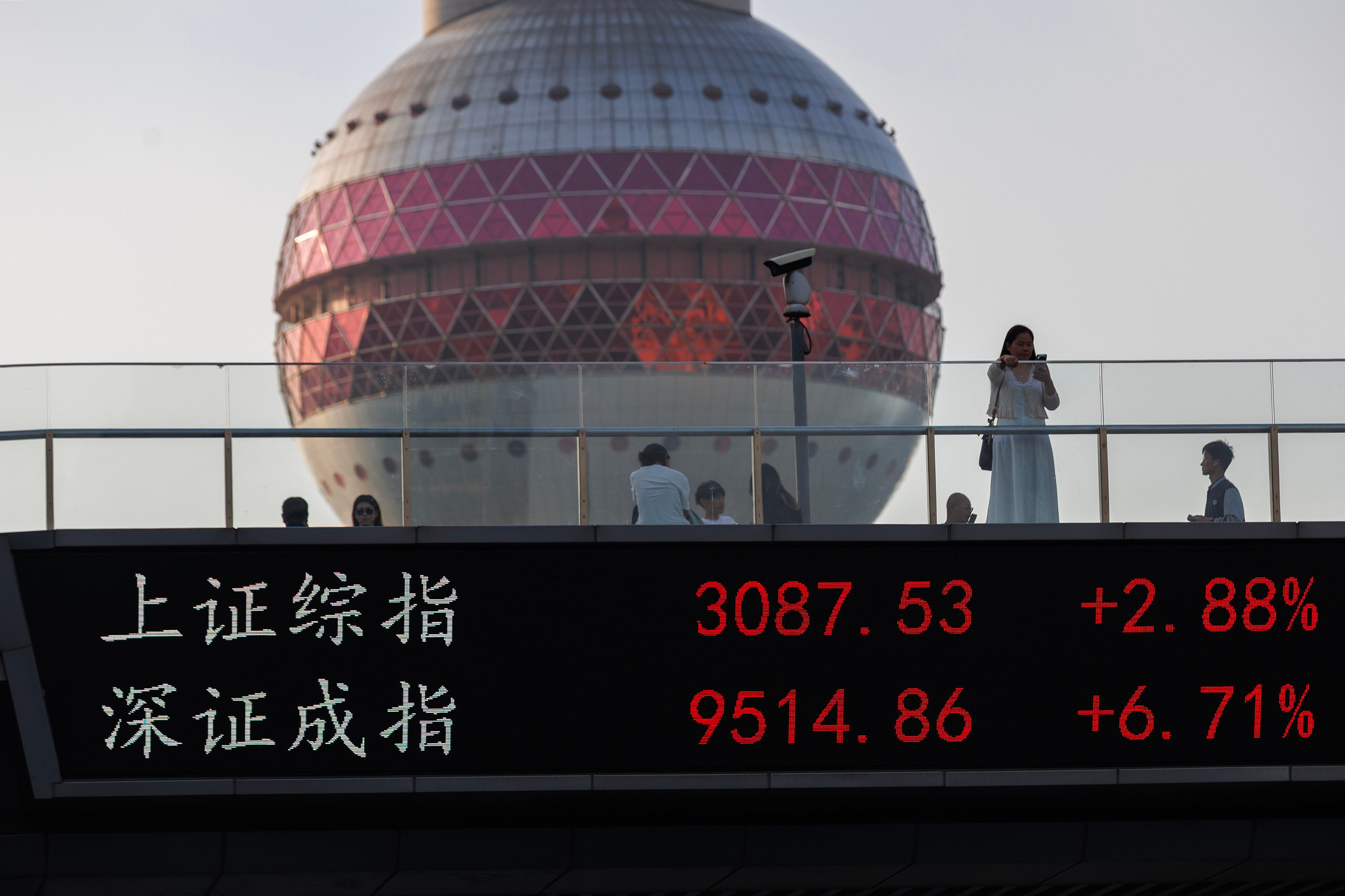 People walk on a pedestrian bridge that displays the stock prices from the Shanghai and Shenzhen exchanges on September 27, 2024 in Shanghai. Photo: Getty Images