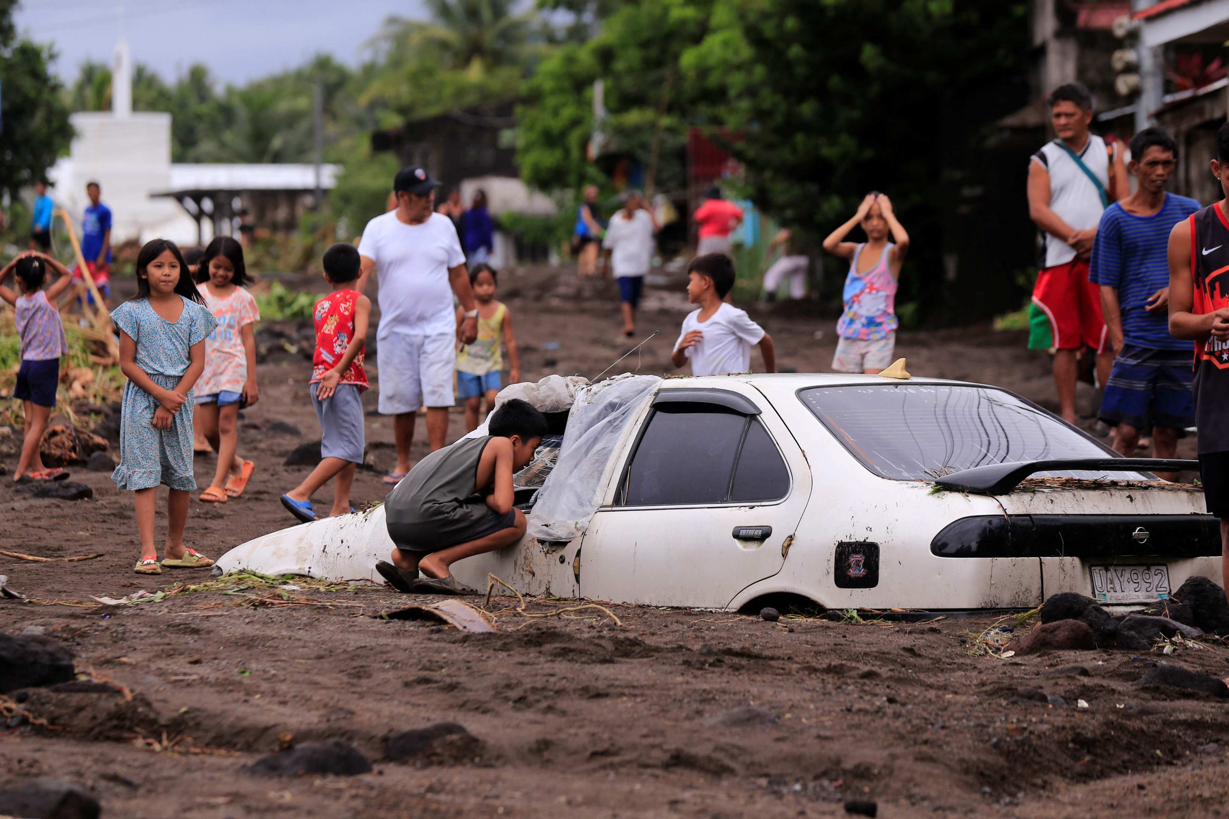 Residents look at a car buried by volcanic ash which cascaded into a Philippine village triggered by heavy rains sparked by Tropical Storm Trami in Guinobatan town, Albay province, on Wednesday. Photo: AFP