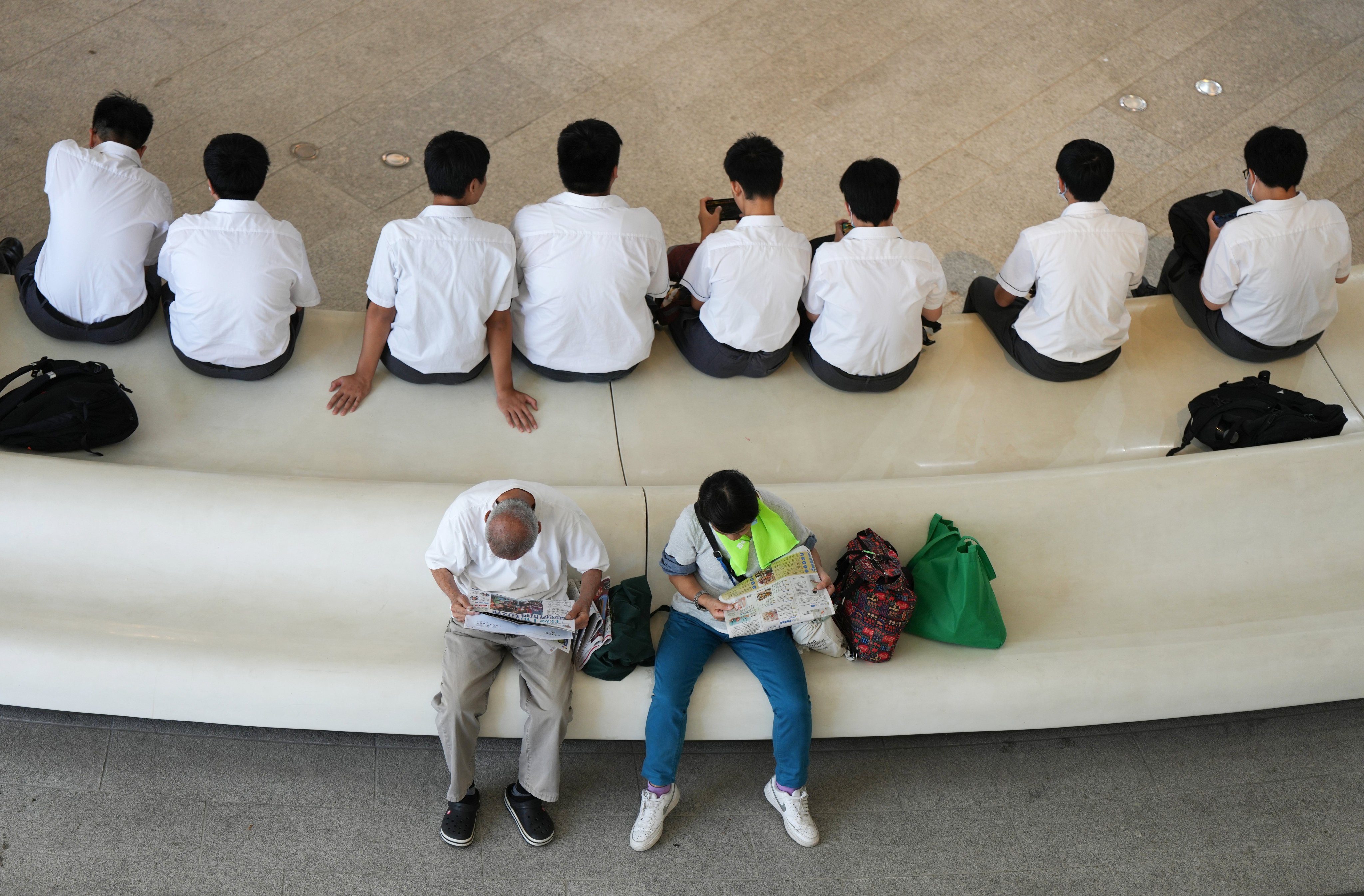 Students look at their phones while two elderly people read newspapers on a bench in Tsim Sha Tsui, Hong Kong. Photo: Eugene Lee