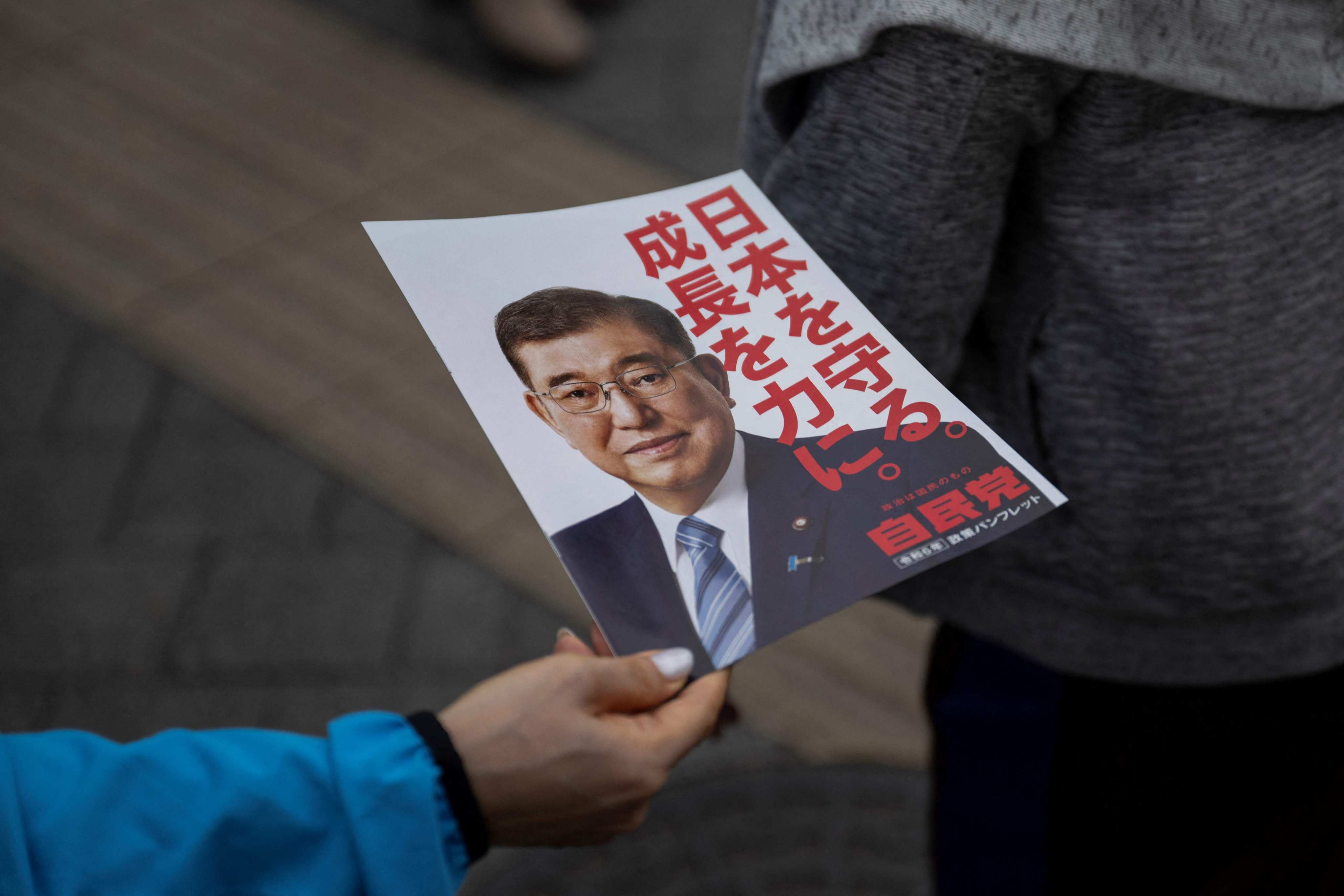 A member of staff hands flyers out with the picture of Japan’s Prime Minister, Shigeru Ishiba, before his election campaign speech in Tokyo on Saturday. Photo: AFP