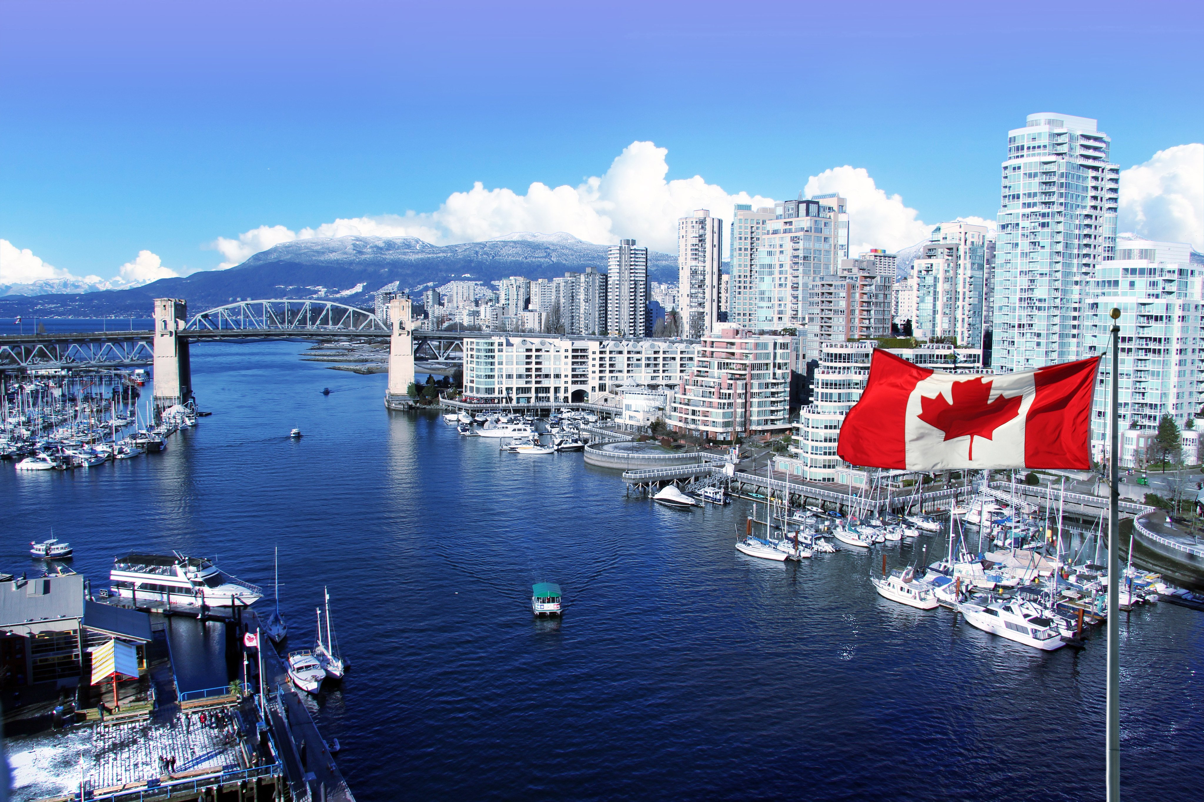 A Canadian flag waves in front of a view of False Creek and the Burrard street bridge in Vancouver, Canada. Photo: Shutterstock