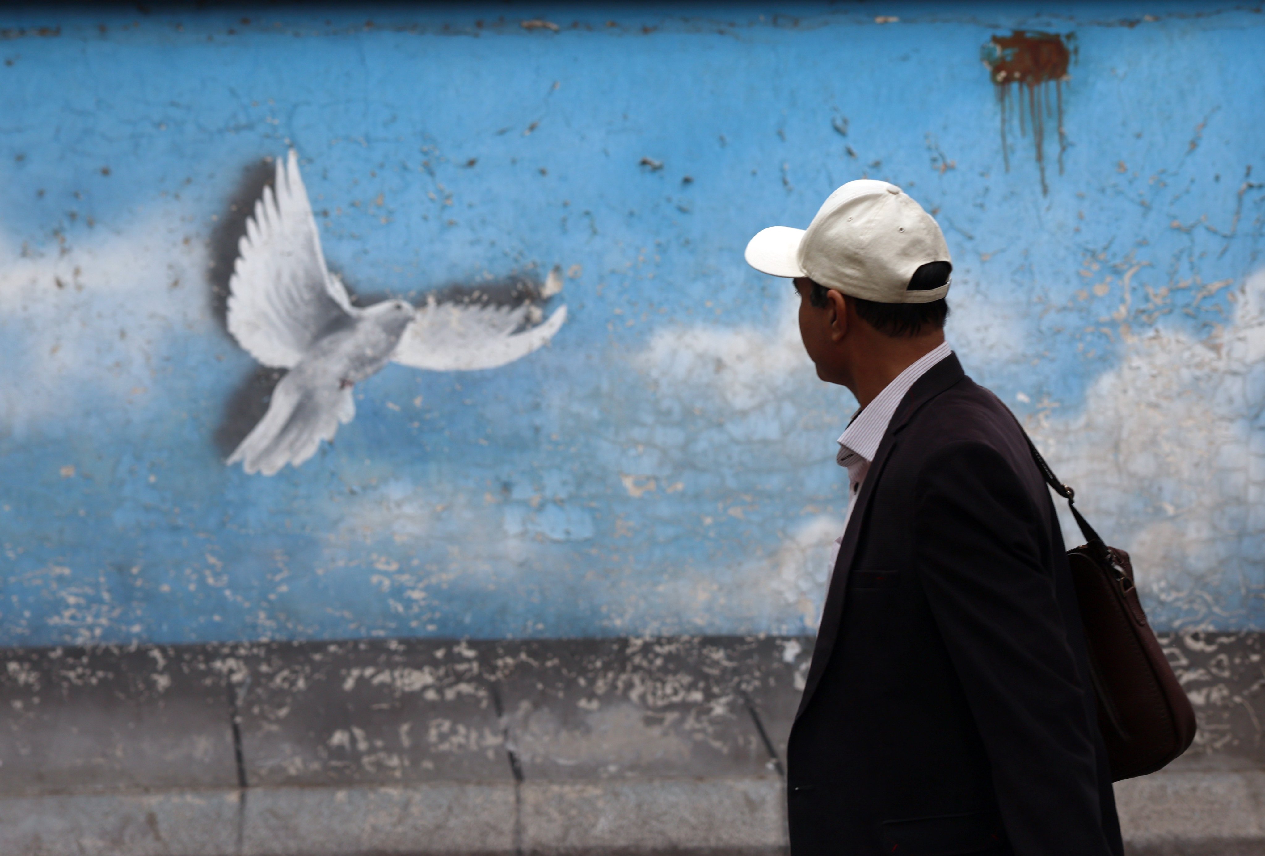 An Iranian man walks past a wall painting of a peace bird in Tehran. Photo: EPA-EFE