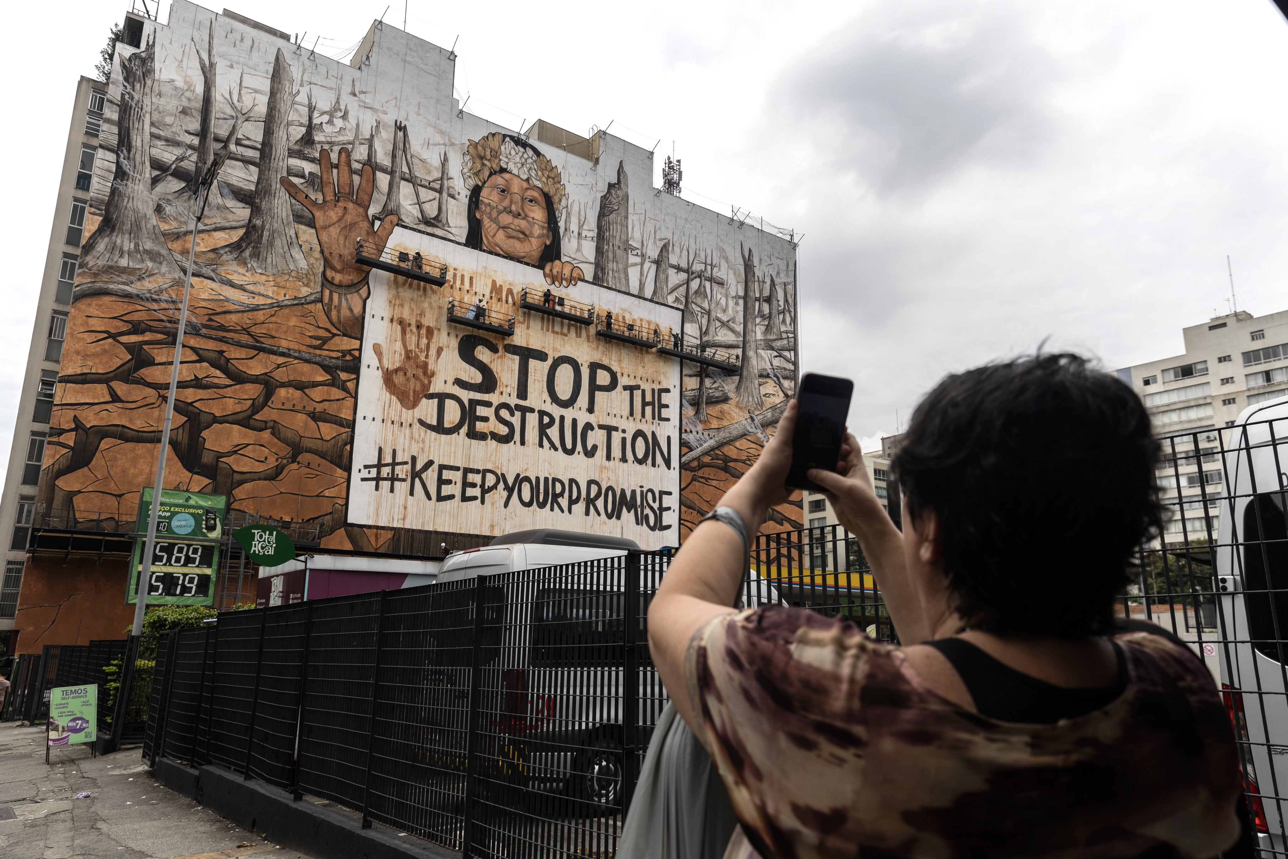 A passerby takes a photo of a mural painted with ashes from the fires ravaging Brazil in Sao Paulo on October 23. The huge mural by Brazilian artist Mundano demands that agricultural companies stop deforestation in the Amazon. Photo: EPA-EFE