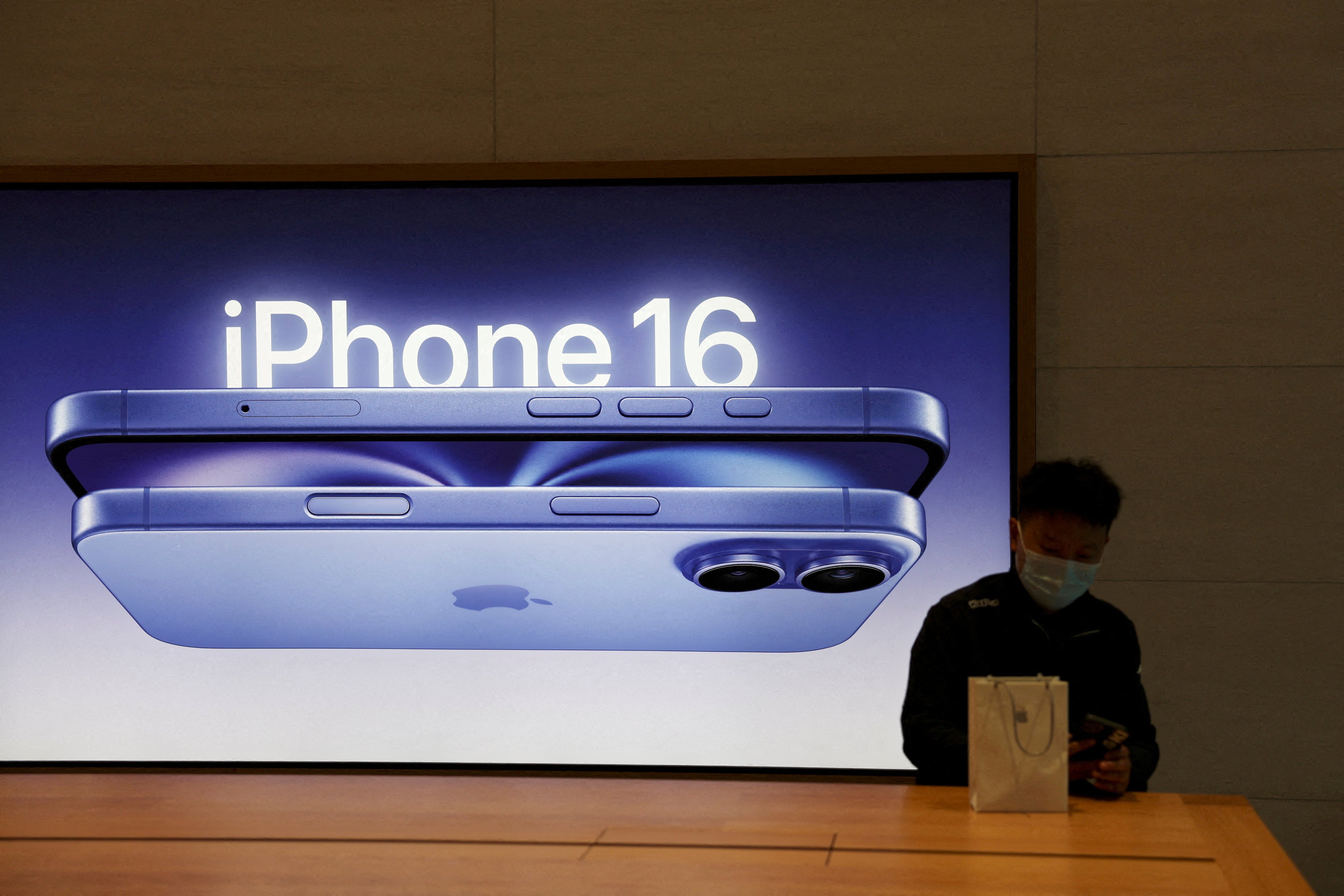 A man sits next to an iPhone 16 advertisement as the new smartphones go on sale at an Apple store in Beijing on September 20. Photo: Reuters