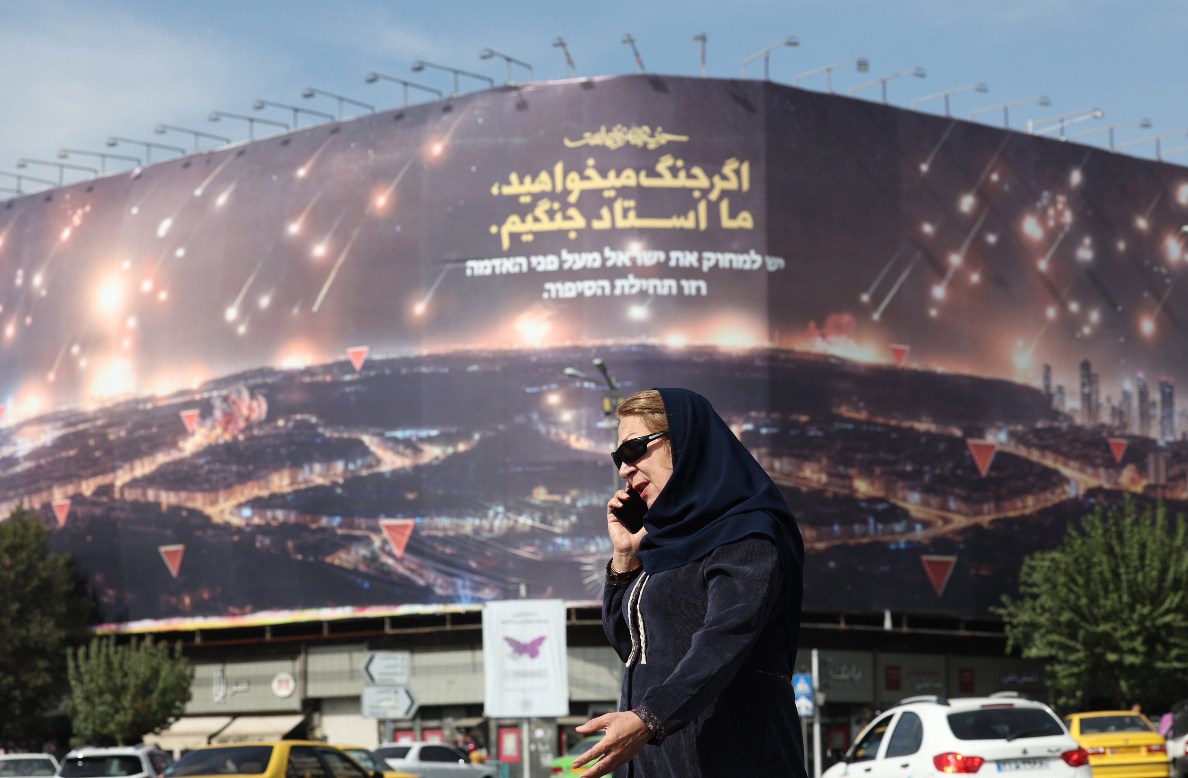 A woman walks past an anti-Israel hoarding in Tehran on October 26 depicting Iran’s recent missile attack on Israel and a sentence reading in Persian: “If you want war, we are the master of war.” Photo: EPA-EFE