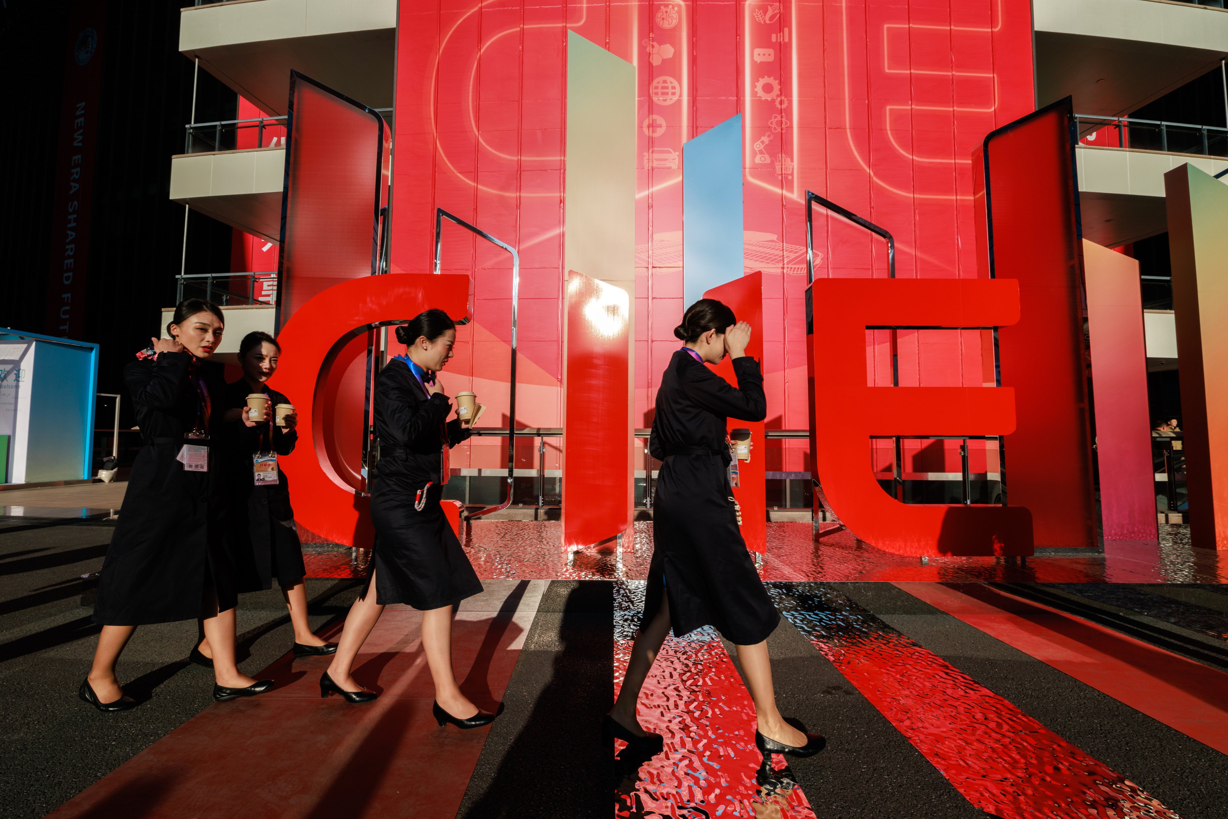 Hostesses for the China International Import Expo walk past a signage of the trade fair in Shanghai. Photo: EPA-EFE