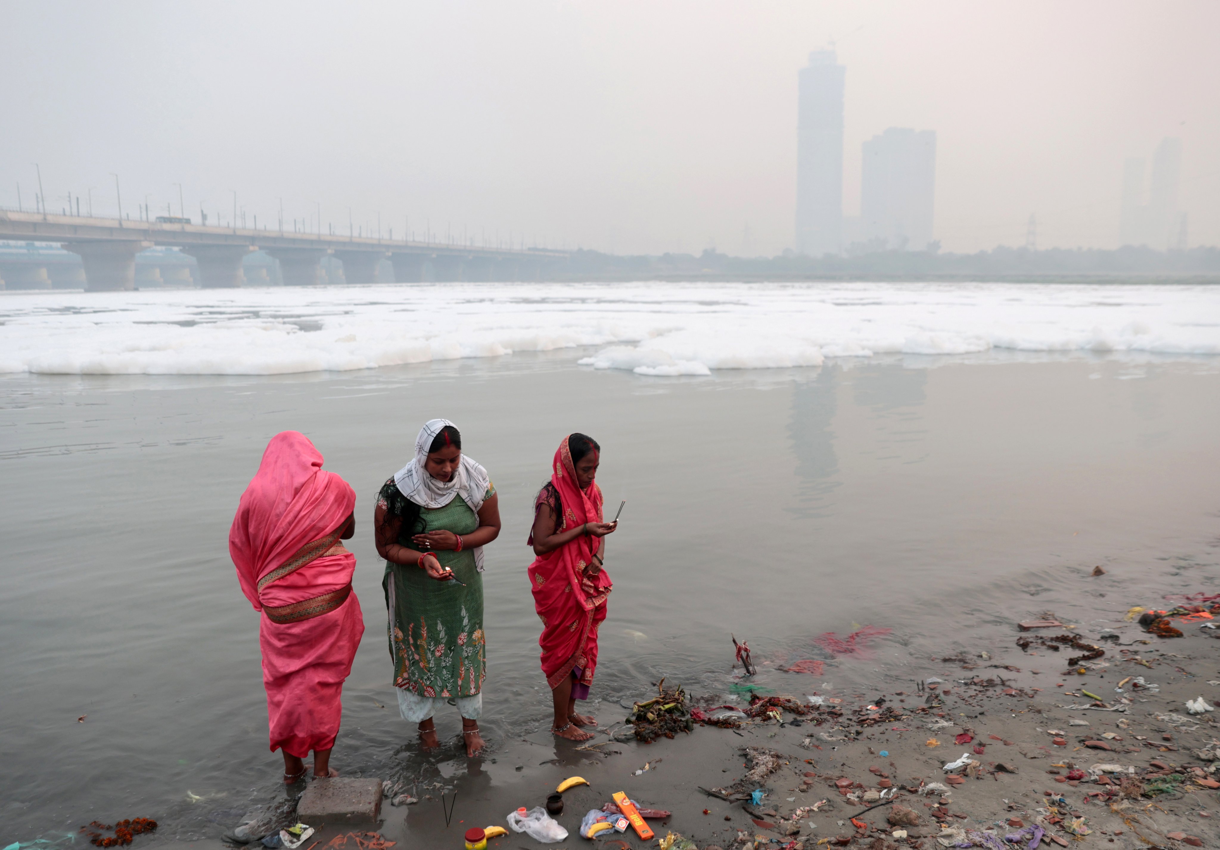 Indian women perform morning rituals while toxic foam caused by industrial waste floats on the surface of the Yamuna river. Photo: EPA-EFE