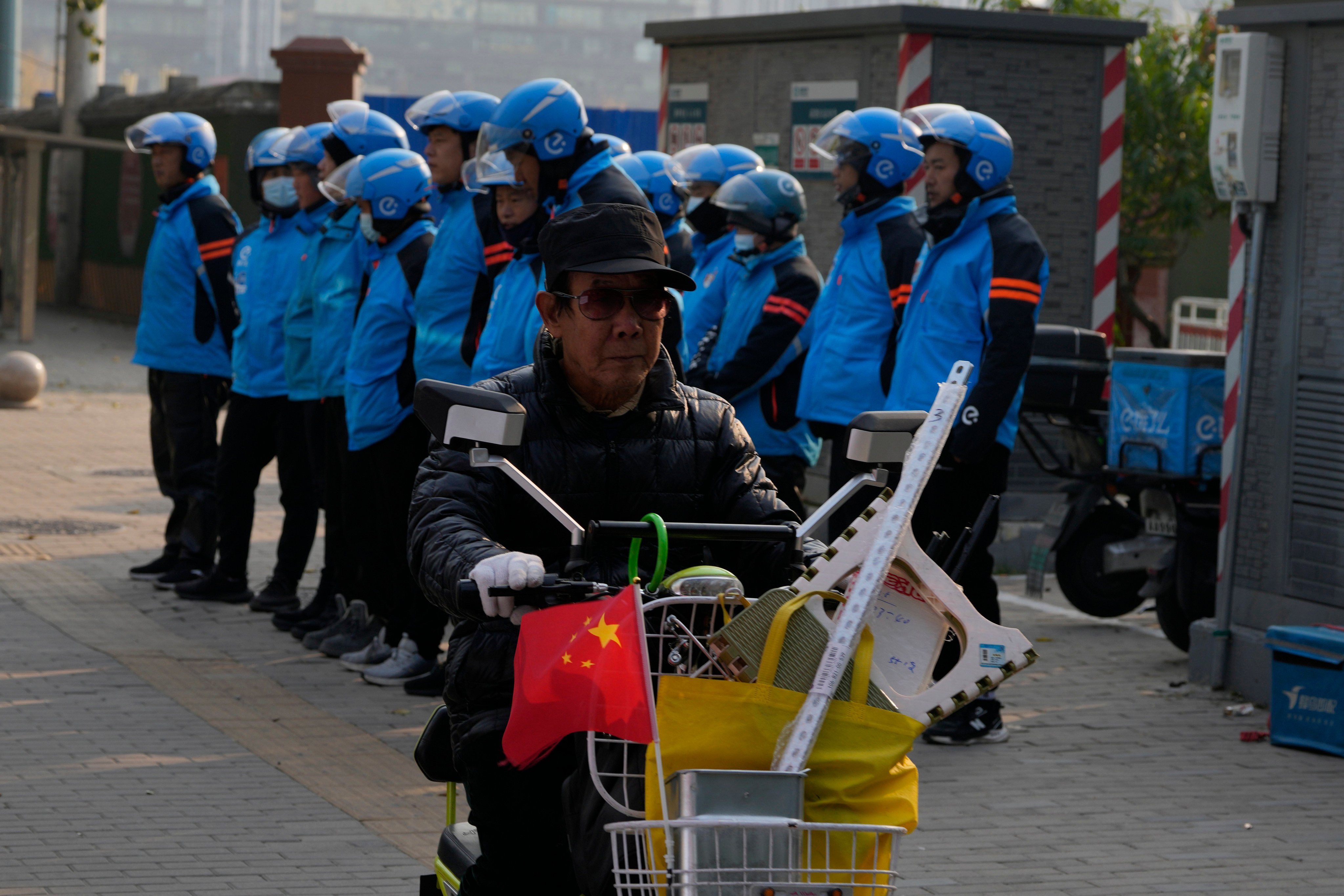 A worker rides past food delivery couriers preparing for the lunch hour in Beijing. Photo: AP