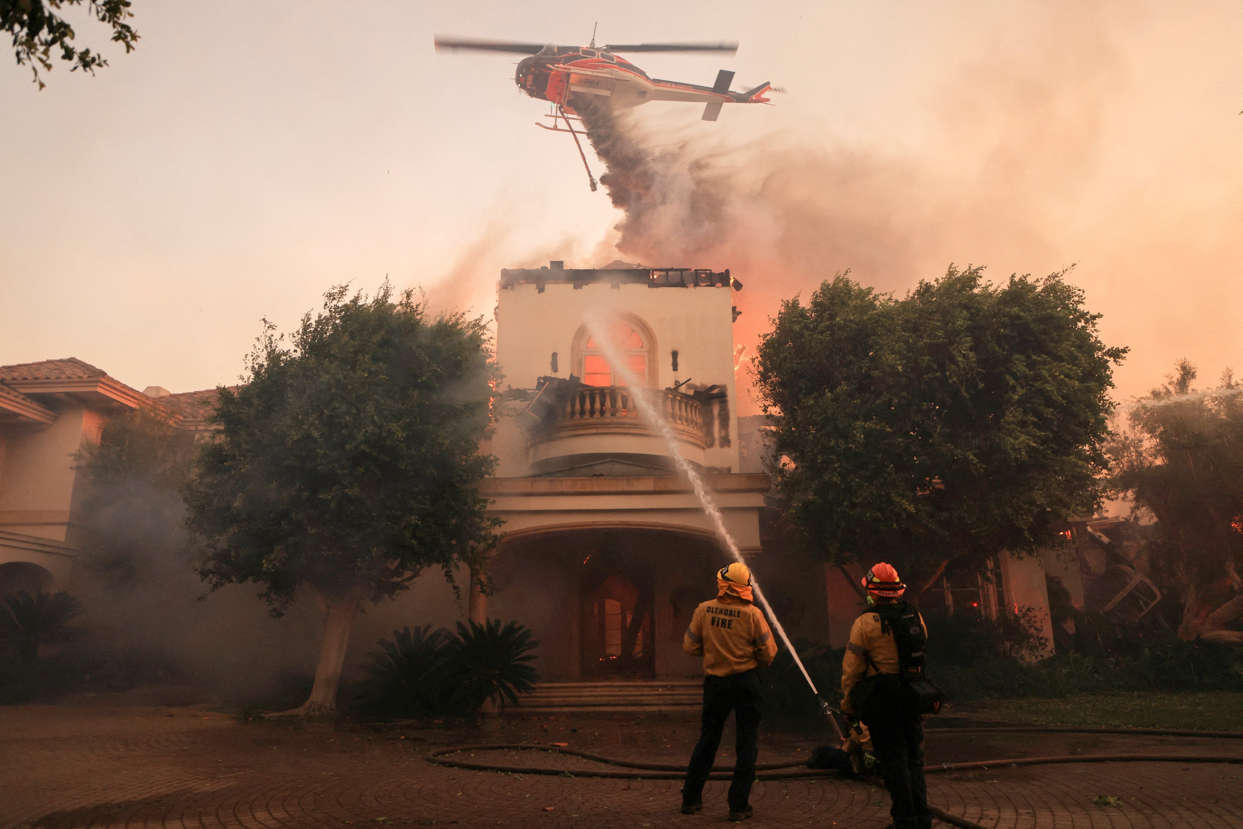 Firefighters try to stop a fire in a building while a helicopter drops retardant in Camarillo, California. Photo: Reuters