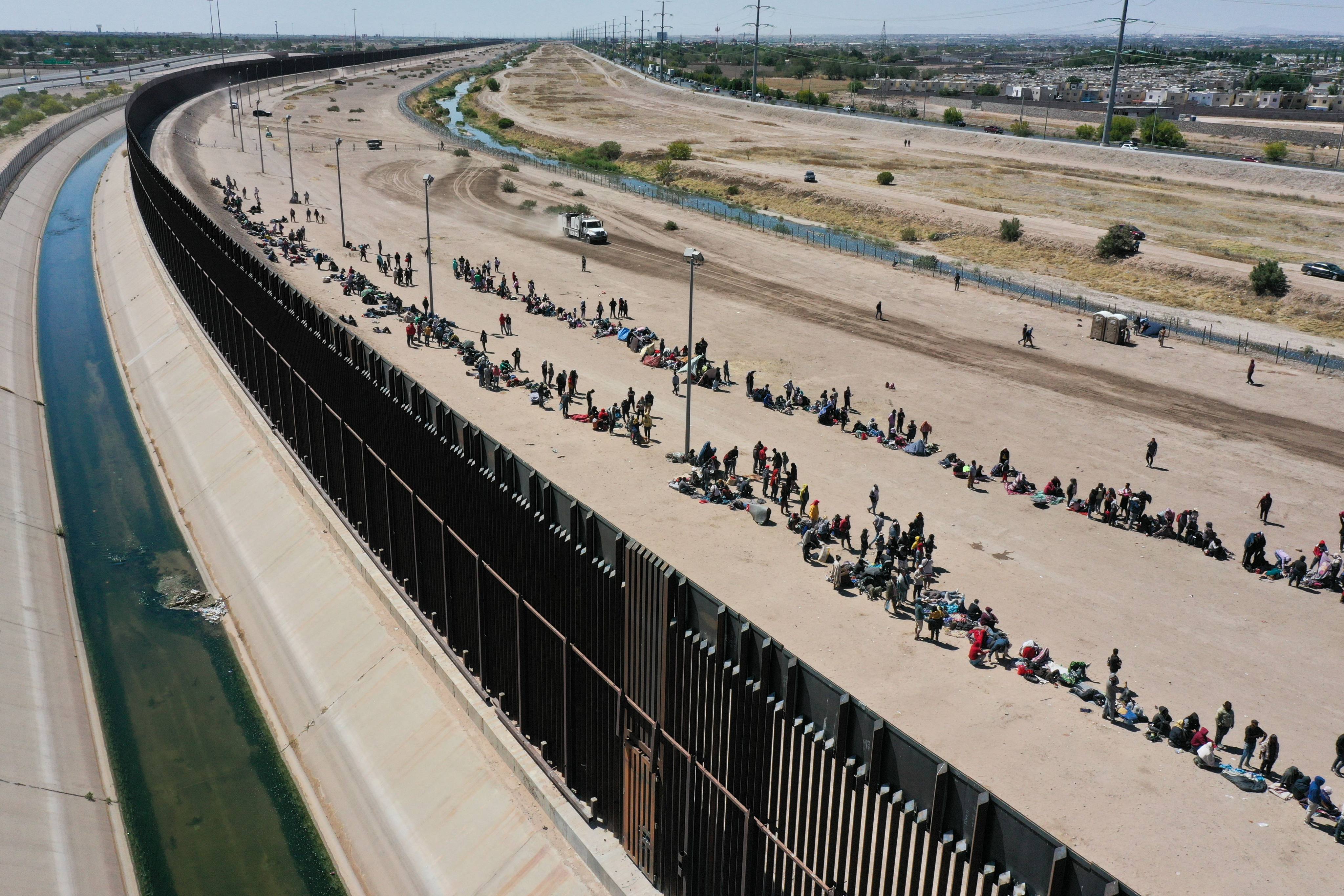 Migrants wait along the US-Mexico border wall in Texas to surrender to American Customs and Border Protection agents for asylum claim processing. Photo: AFP/Getty Images/TNS