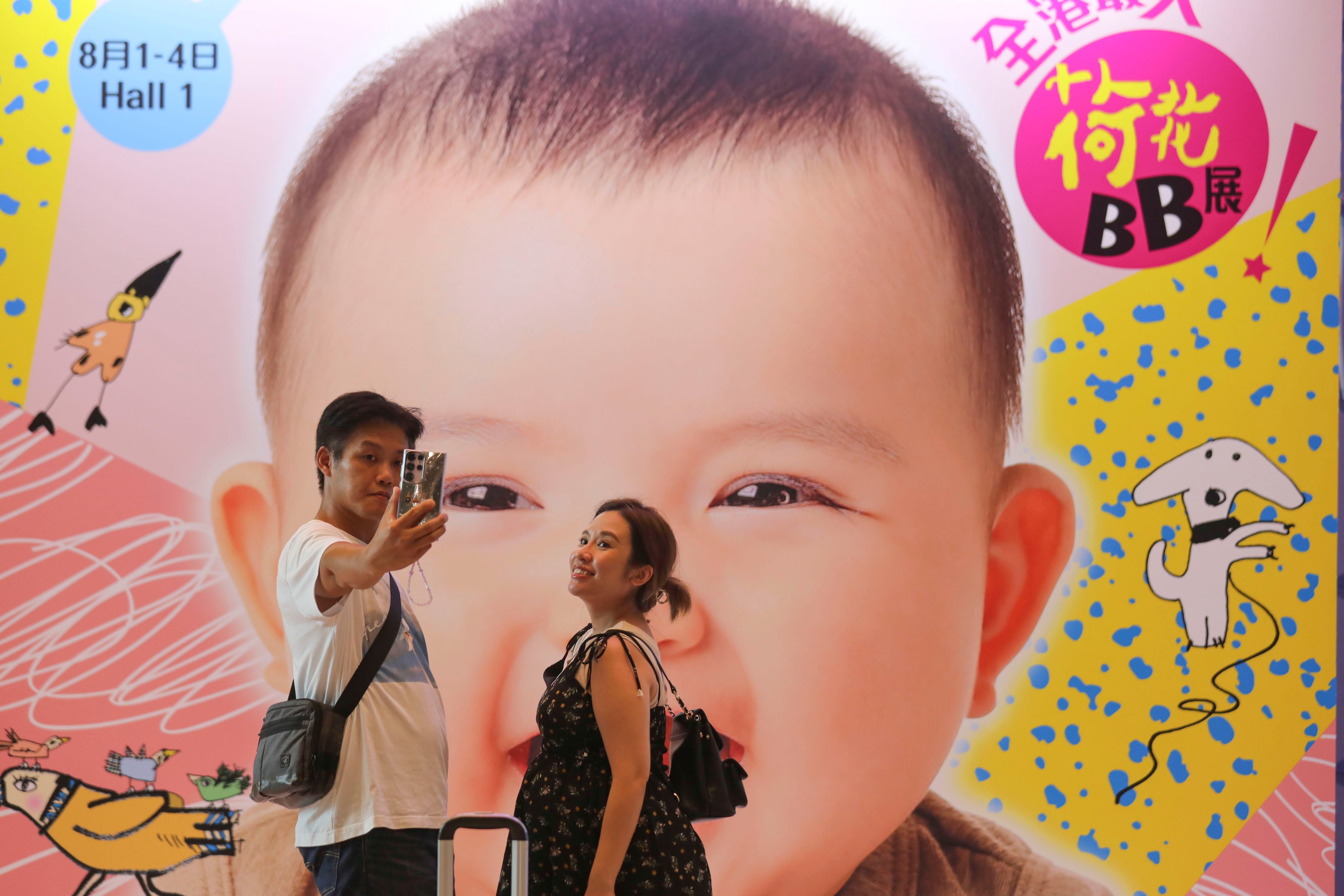 A couple takes a selfie in front of a poster featuring a baby, during an exhibition of children’s products at the Hong Kong Convention and Exhibition Centre in Wan Chai on August 2. Photo: Xiaomei Chen