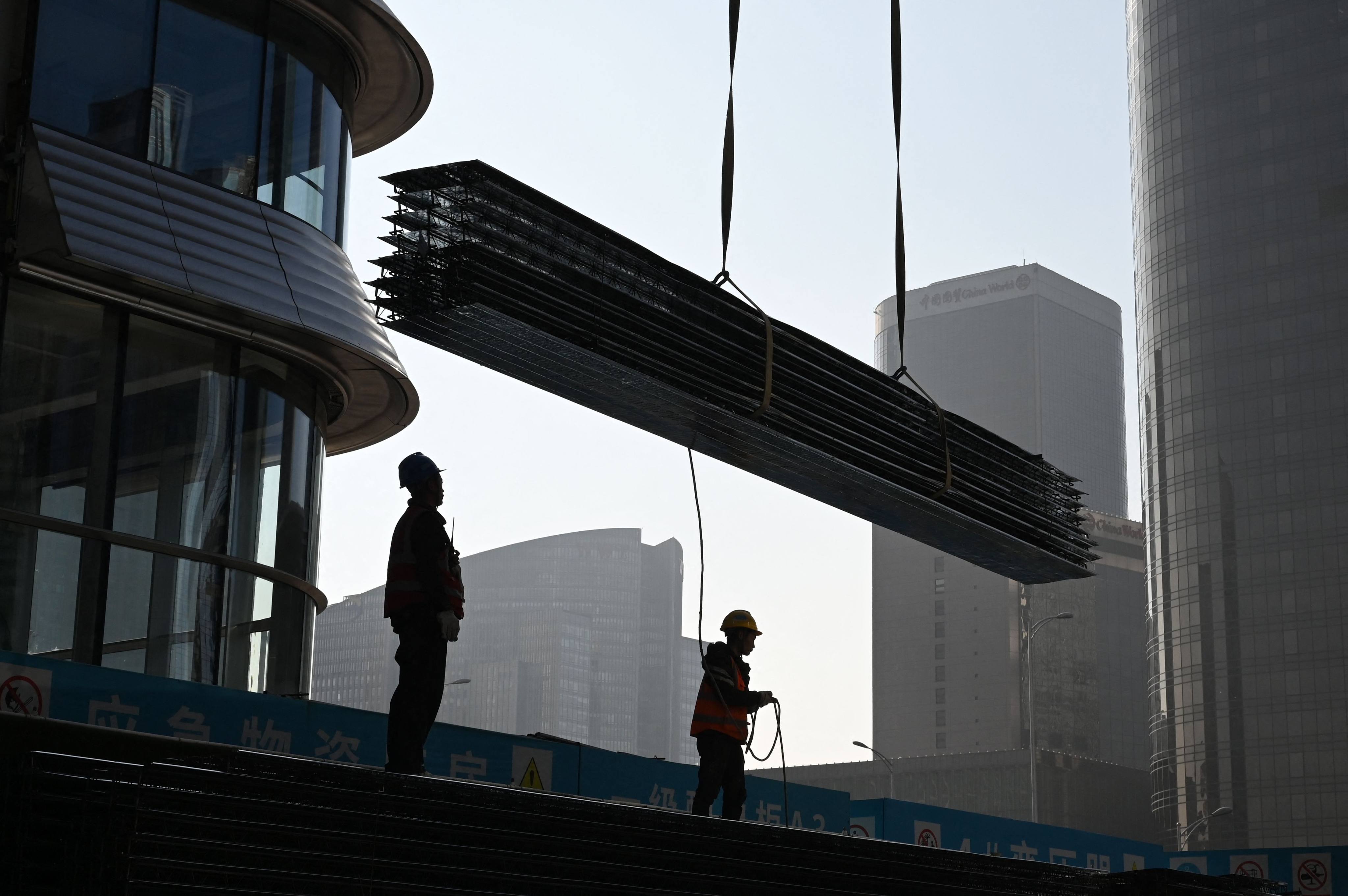 Workers watch as equipment is lifted by a crane on a construction site in the central business district in Beijing. Photo: AFP