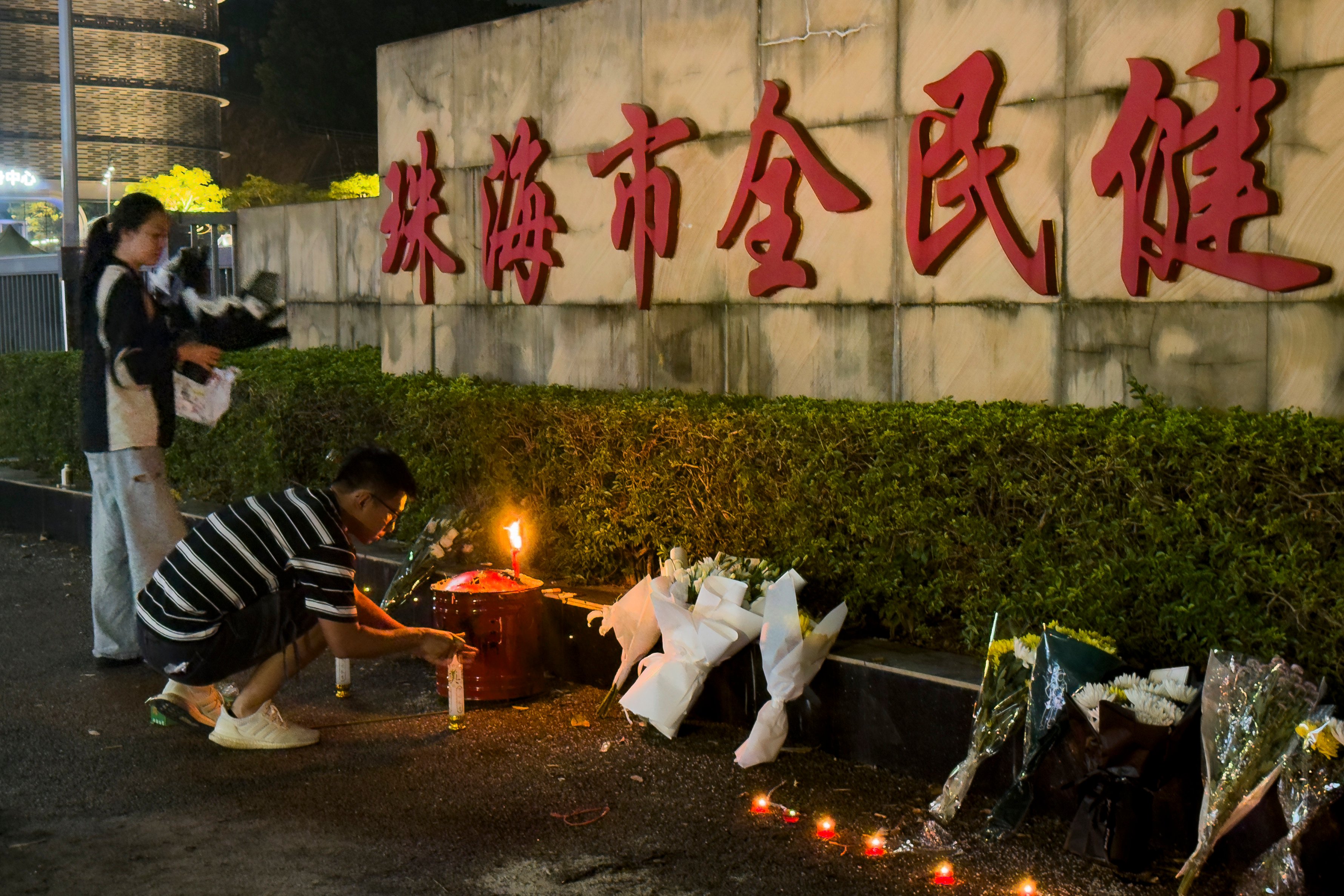 A man lights a candle near flowers placed outside a Zhuhai sports centre on Tuesday where a car driver deliberately rammed  into people exercising a day earlier. Photo: AP
