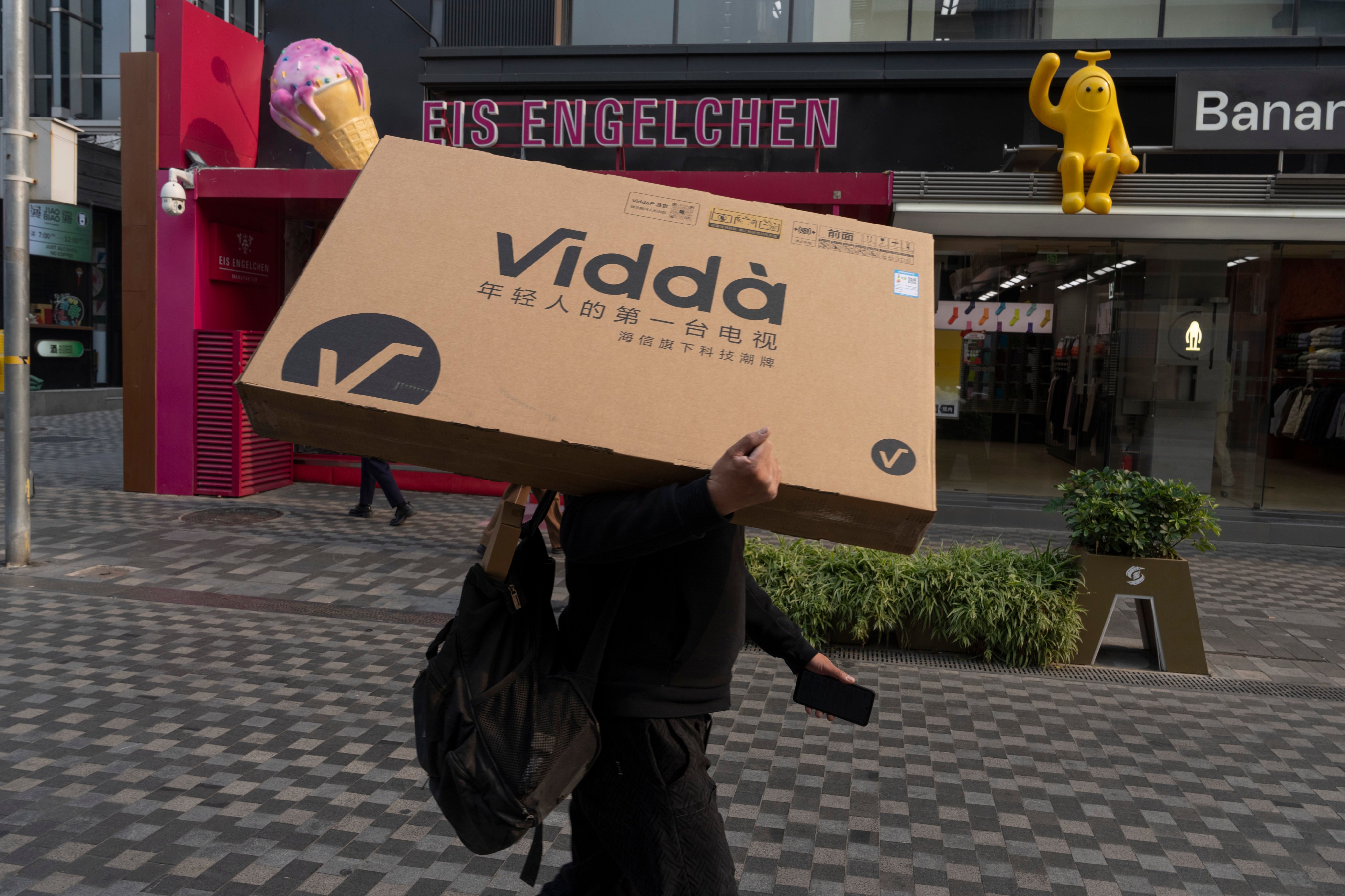 A man carries a television set on his shoulder as he passes through the Sanlitun shopping district in Beijing. Photo: AP