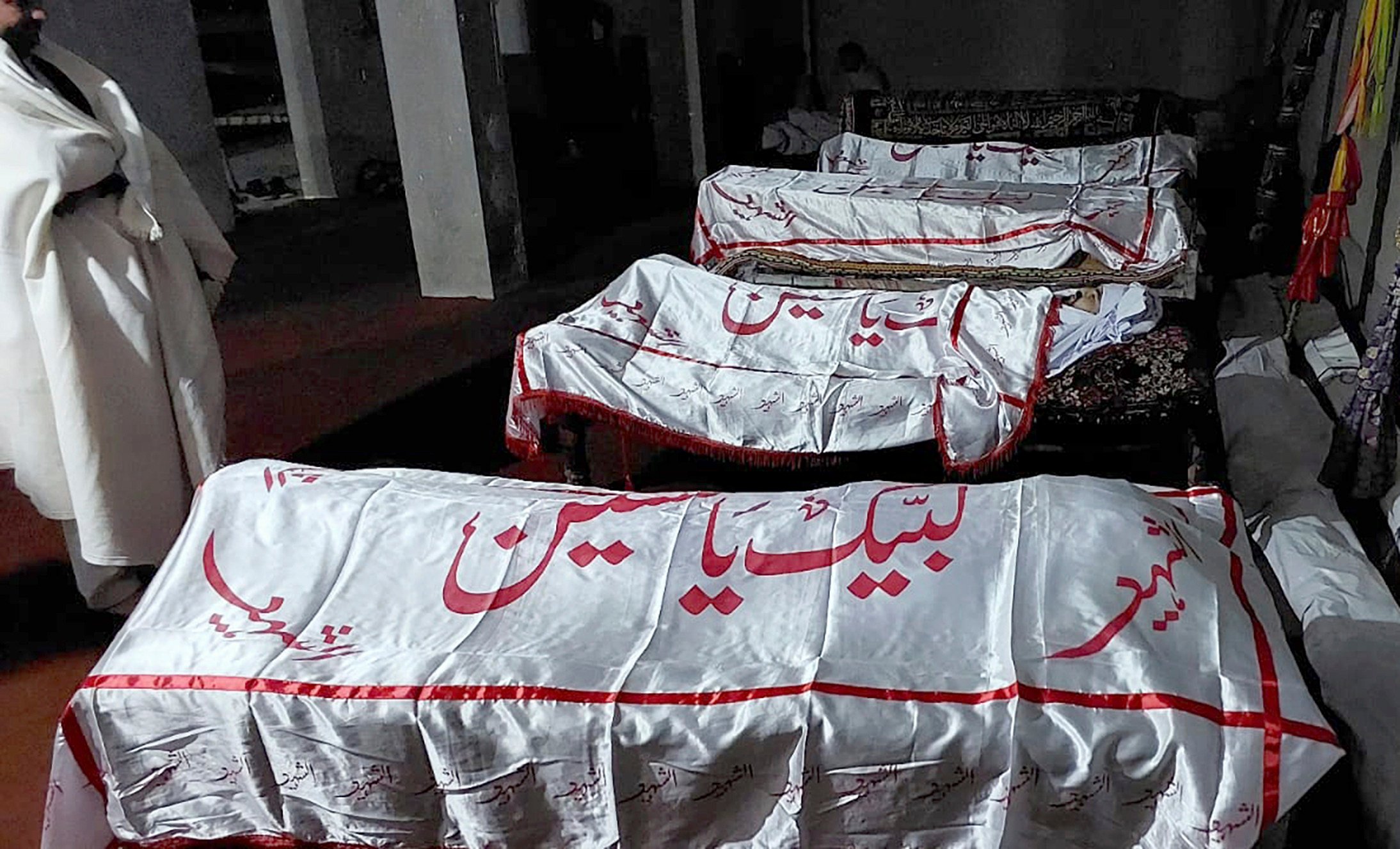 A mourner stands beside the bodies of some of the 40 people killed when gunmen opened fire on a convoy of buses in Pakistan. Photo: AP