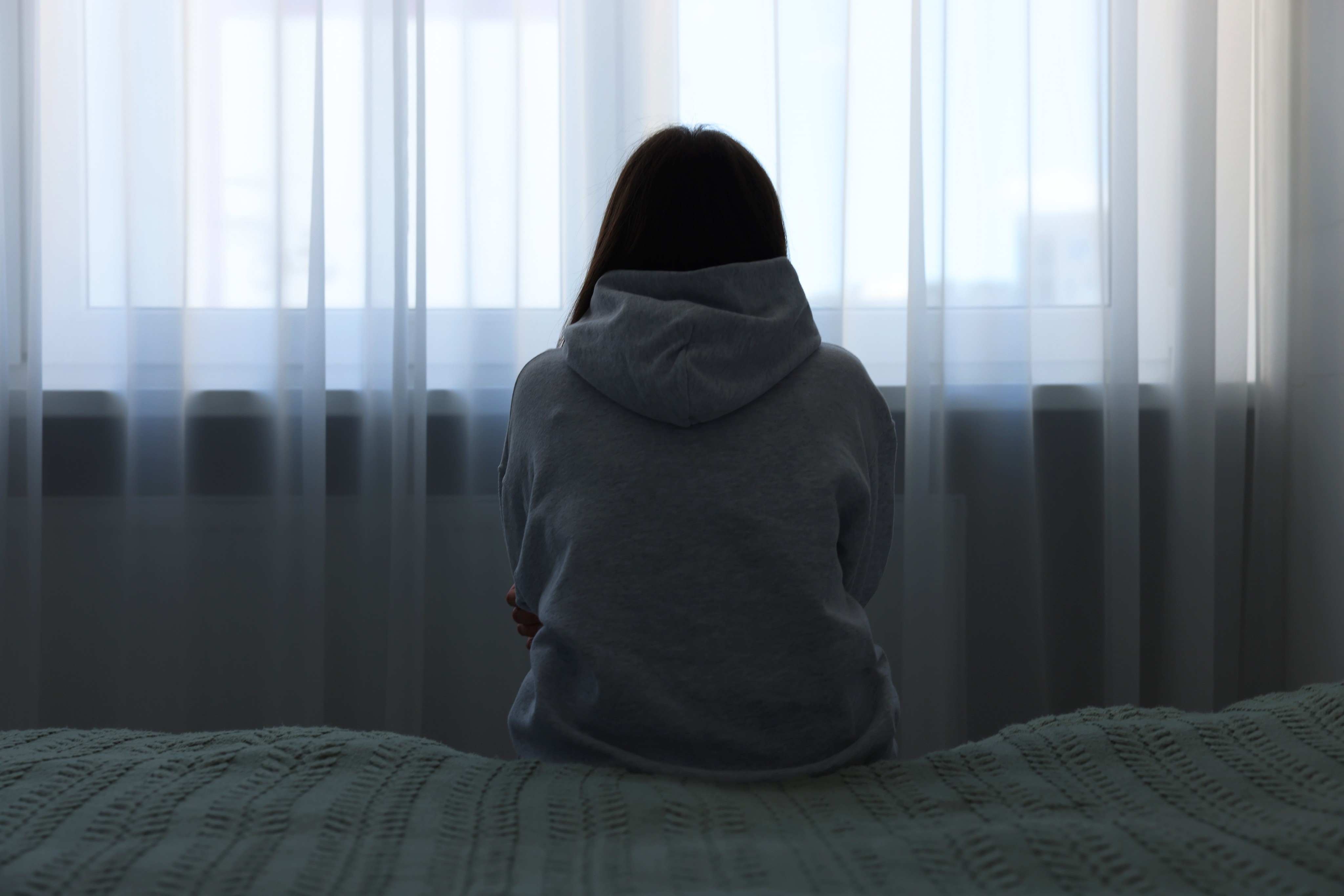 A woman sitting on bed at home. Photo: Shutterstock