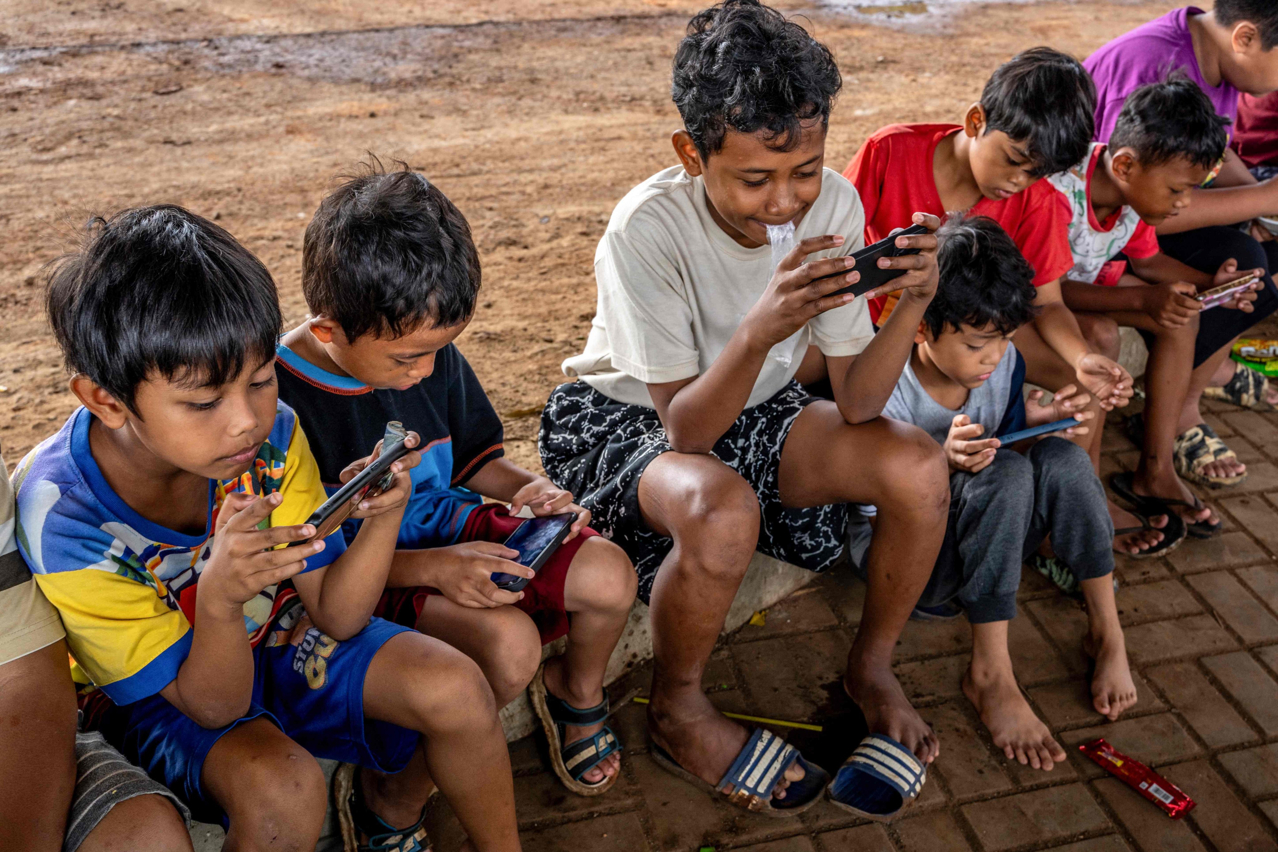 Children look at their mobile phones along a roadside in Jakarta on Wednesday. Photo: AFP