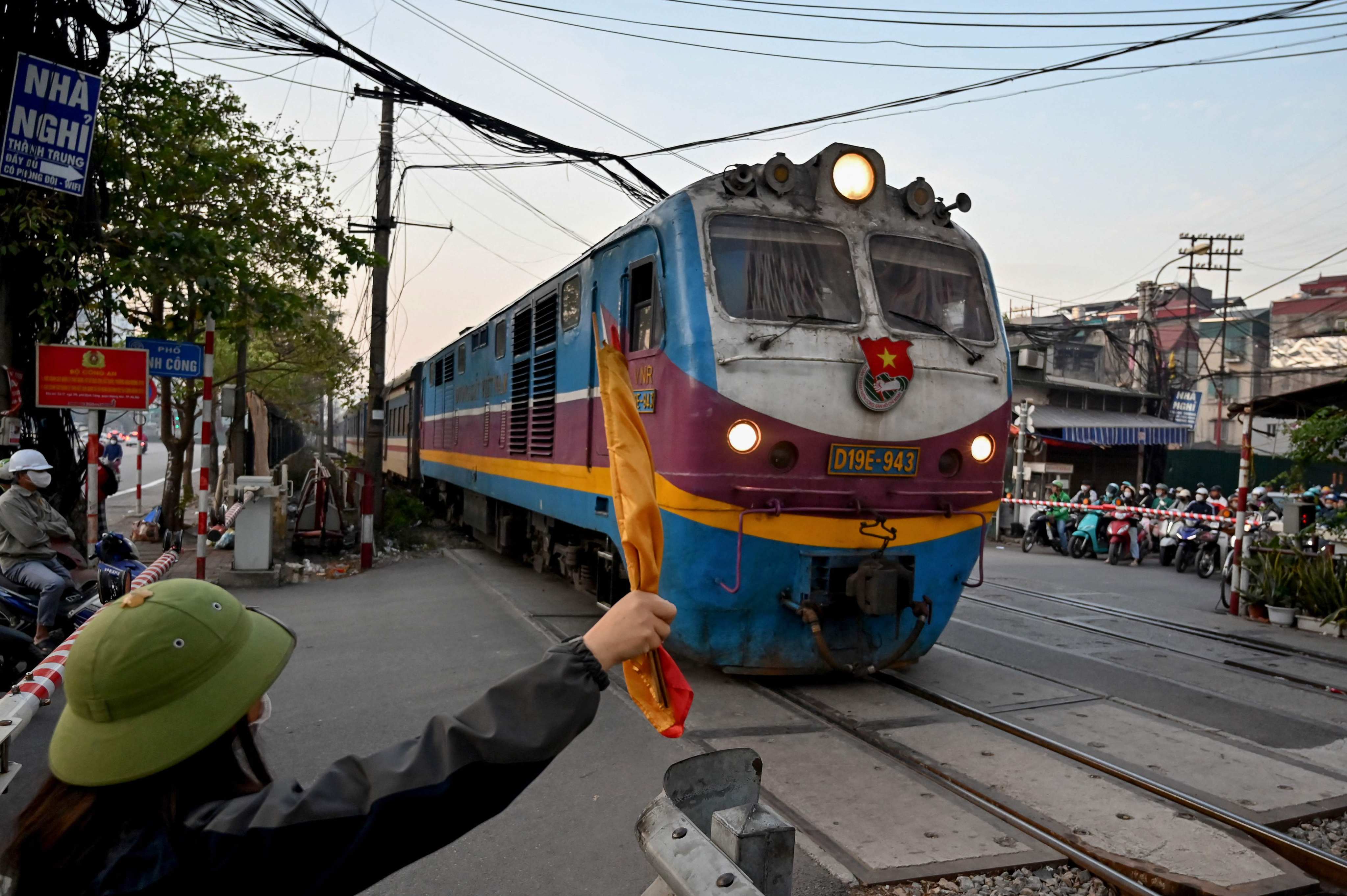 A railway worker holds a flag to signal safety for a passenger train passing through a railway crossing in Hanoi. Photo: AFP